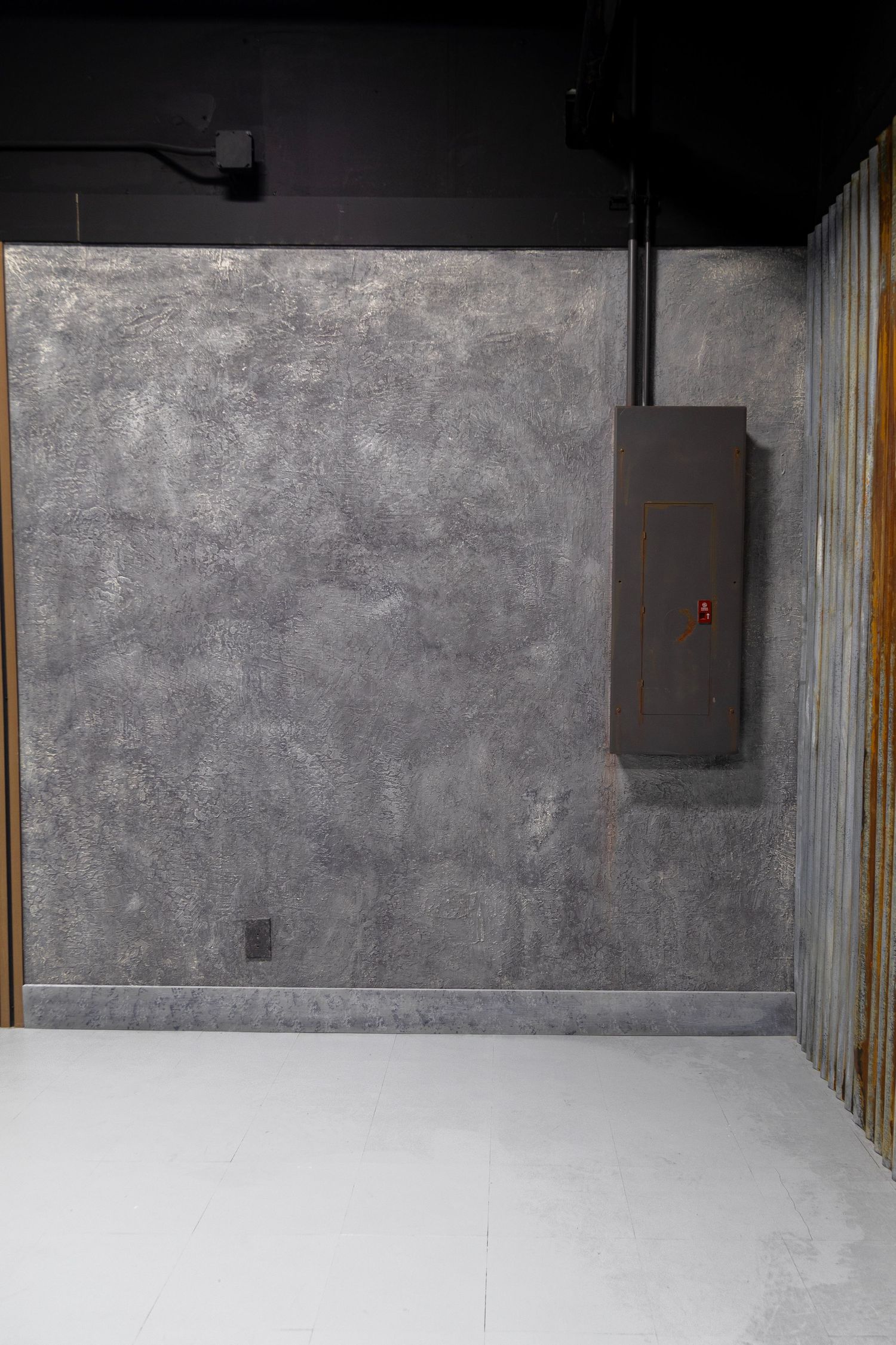 Industrial gray concrete textured studio backdrop wall with black electrical panel and white epoxy floor.