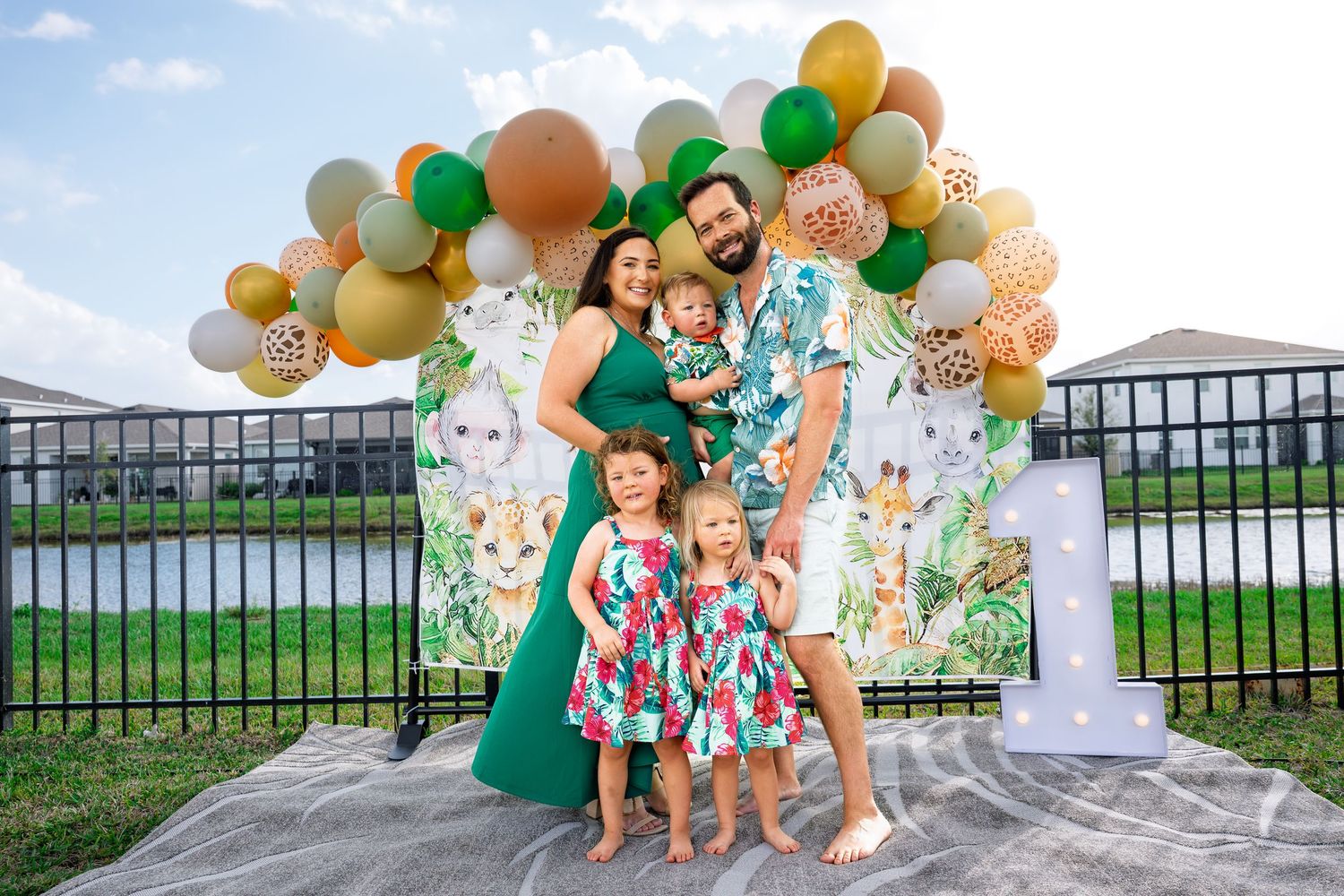 Family of five posing in front of a colorful balloon arch at an outdoor safari-themed birthday party celebration.