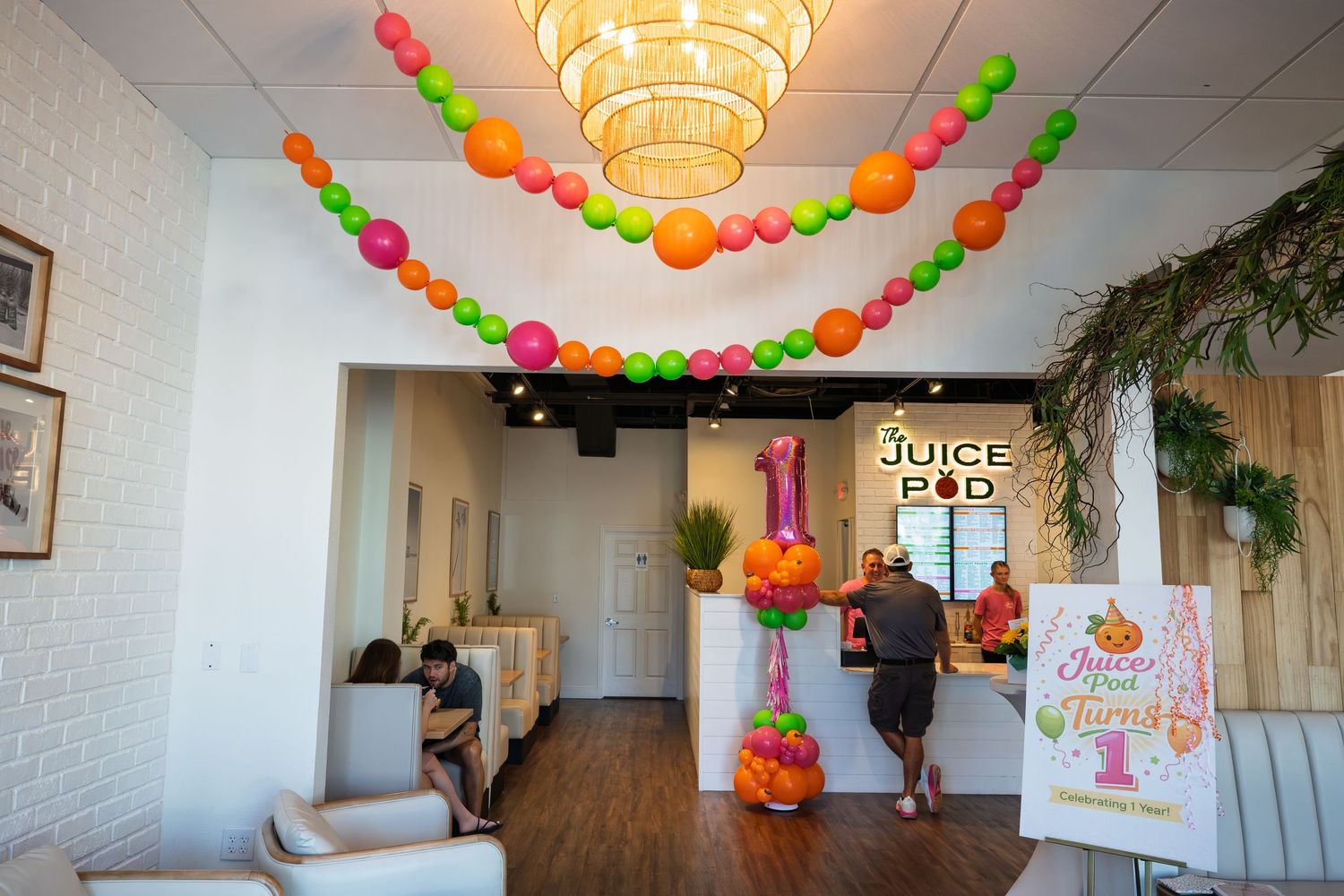 Colorful balloon decorations adorn the ceiling of Juice Pod restaurant during a festive first anniversary celebration event.