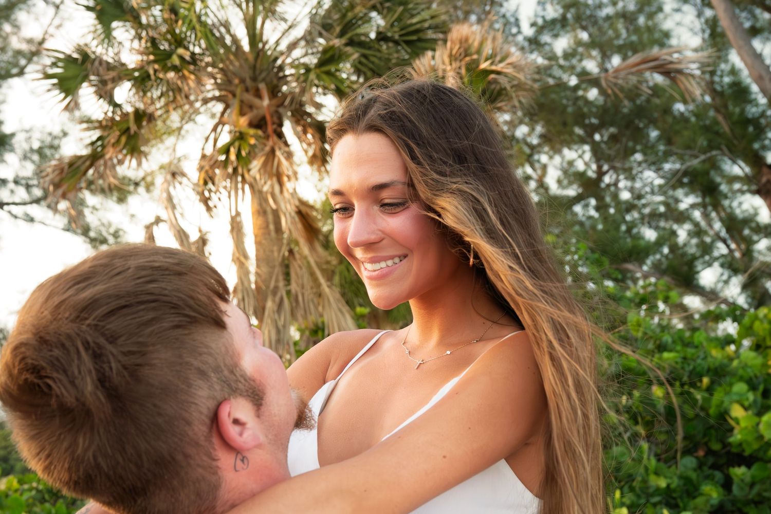 Couple sharing a romantic moment outdoors with tropical palm trees in the background on a sunny day.