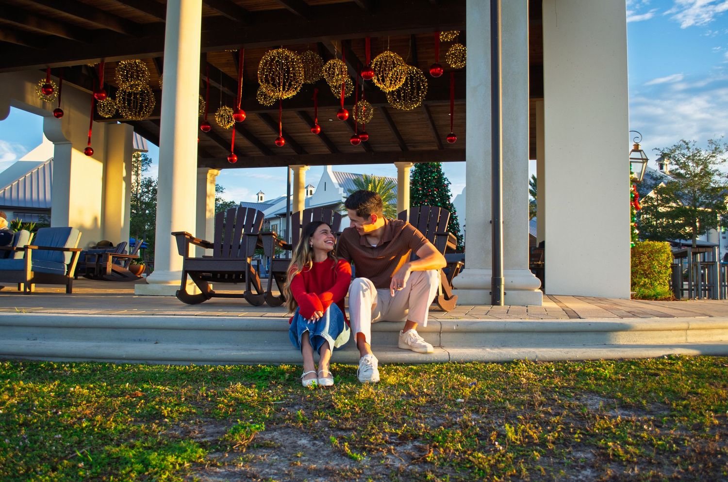 People walk through a covered outdoor walkway on a sunny day with green grass and trees in the background.