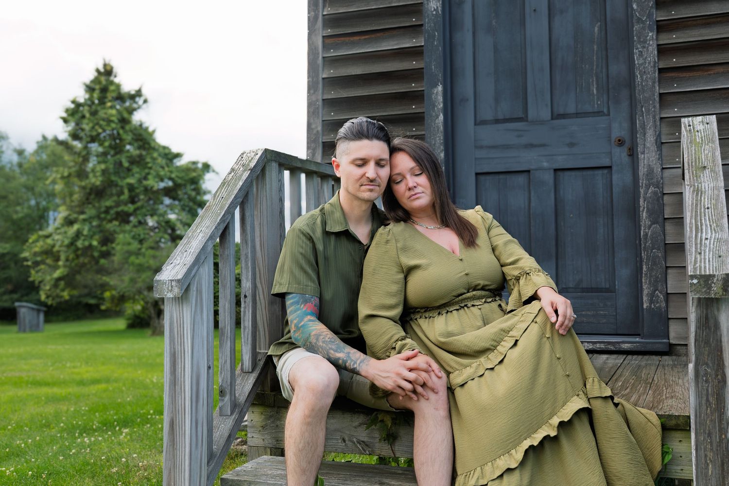 Couple in matching olive green outfits sitting together on rustic wooden steps, leaning close in a tender embrace outdoors.