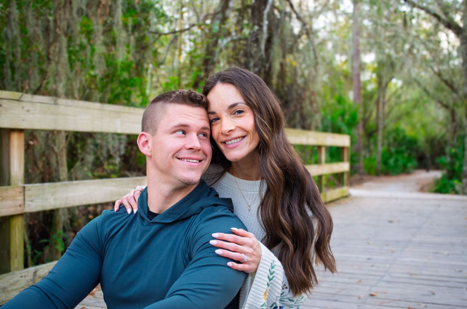 A couple shares romantic moments on a wooden boardwalk surrounded by lush green trees and Spanish moss.