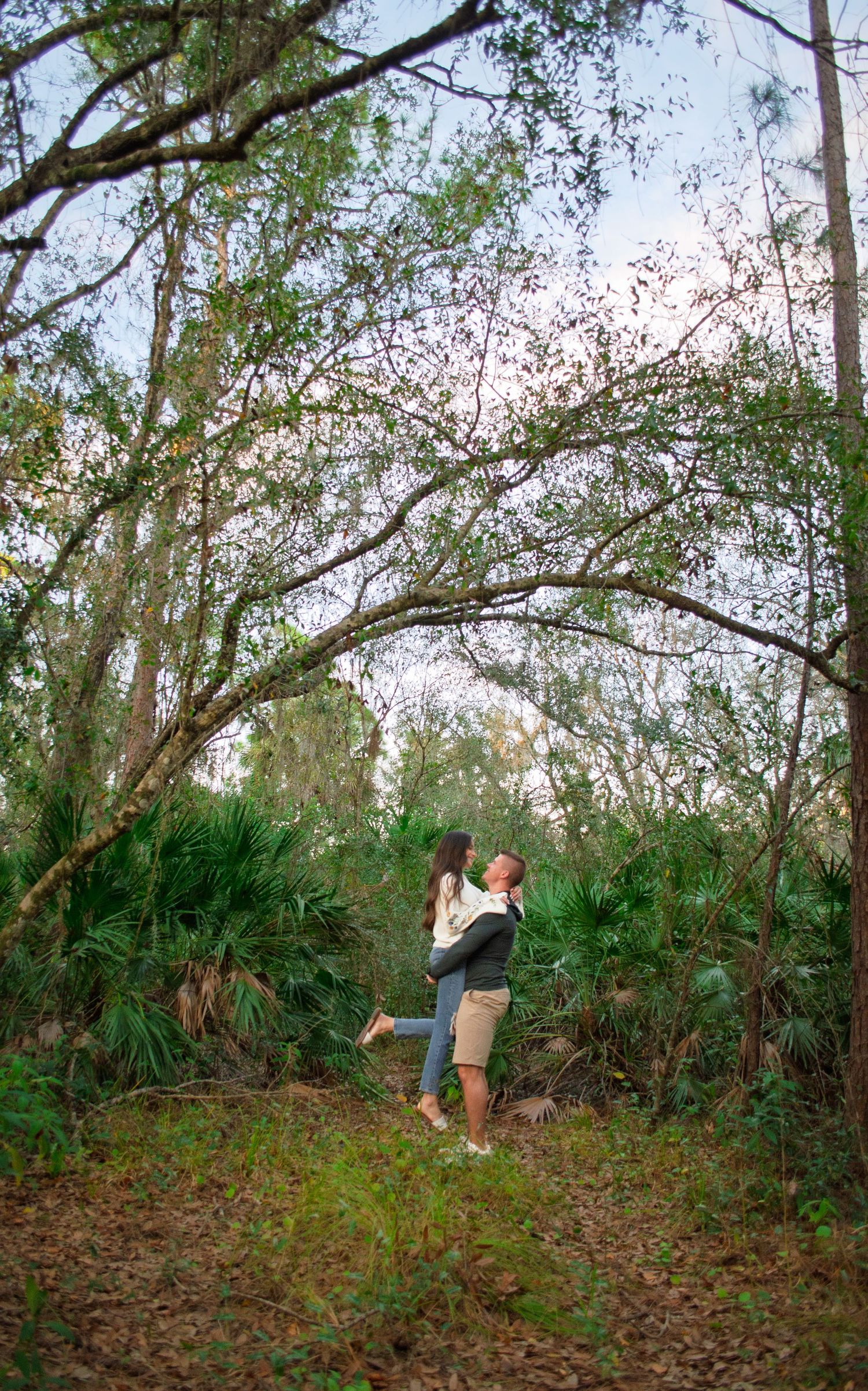 People explore a wooded area with fallen leaves and twisted tree branches in a natural outdoor setting.