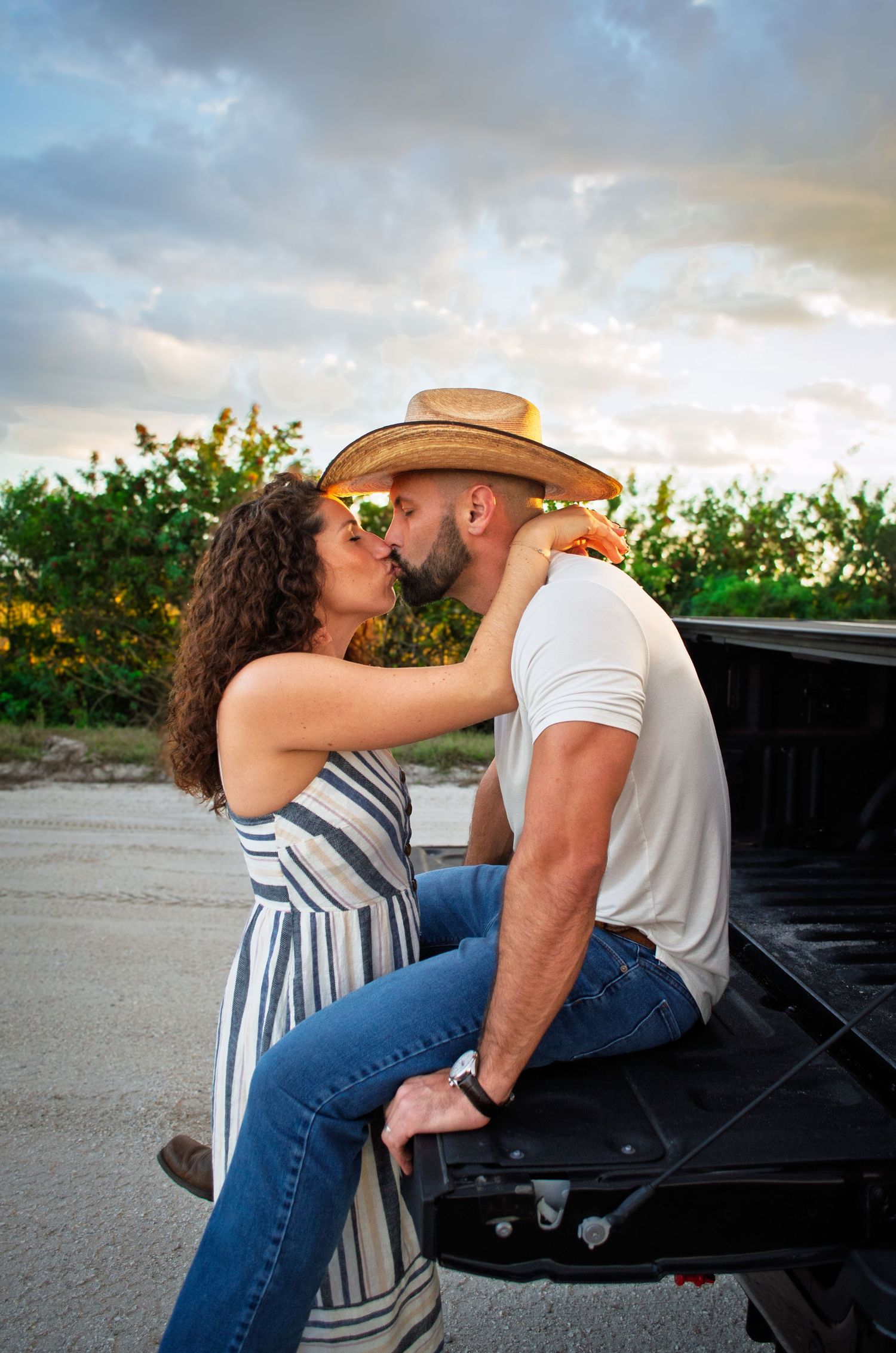 A romantic couple shares a tender moment while sitting on the tailgate of a pickup truck at sunset.