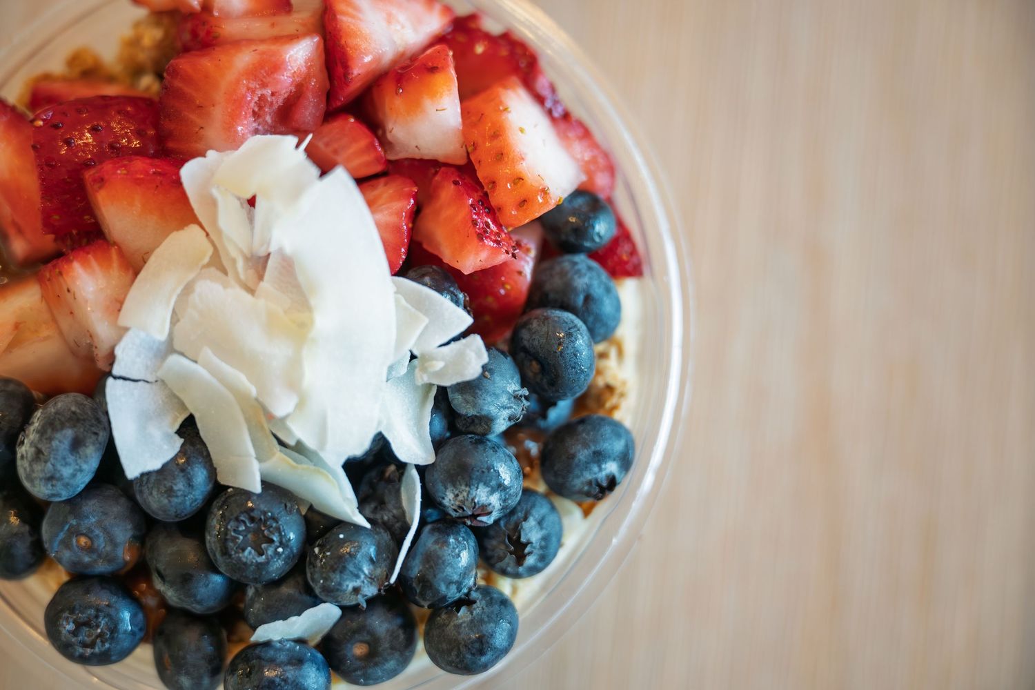 Fresh fruit bowl with blueberries, strawberries, and coconut flakes on granola, served in a clear cup.