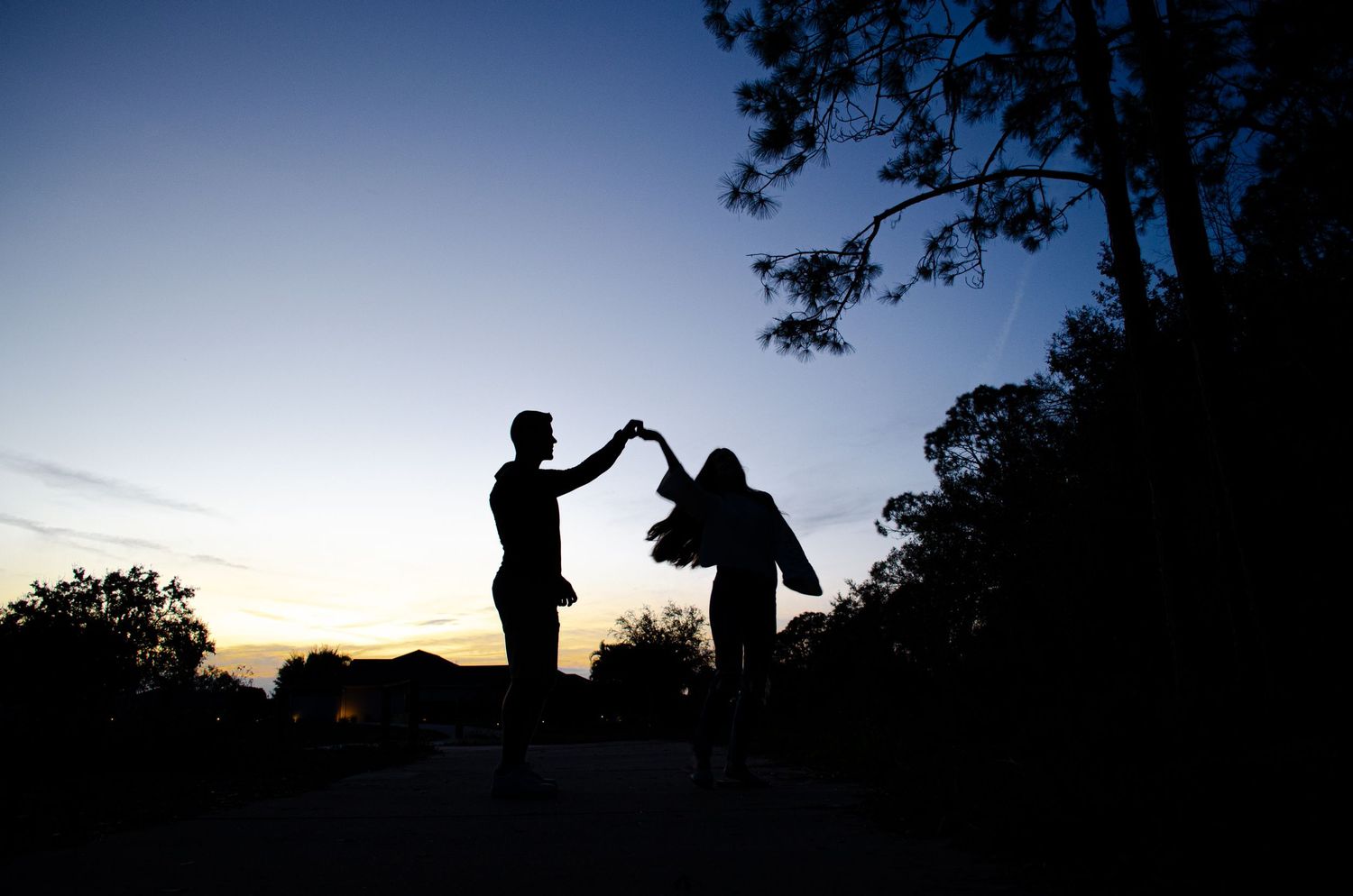 Silhouettes of people and trees against a dramatic sunset sky with dark shadows in the foreground.