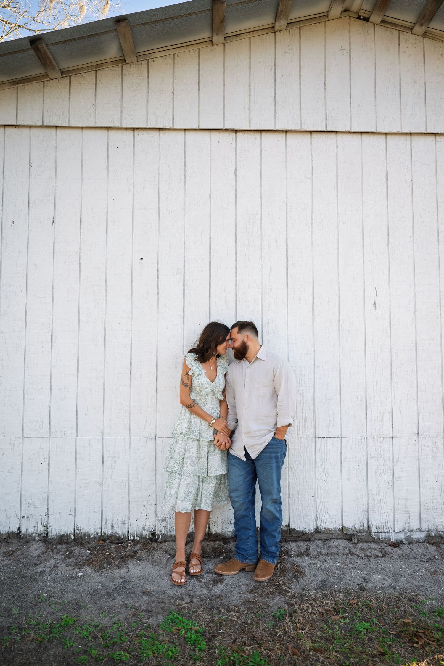 A romantic couple embraces against a white wooden wall in a series of candid poses.