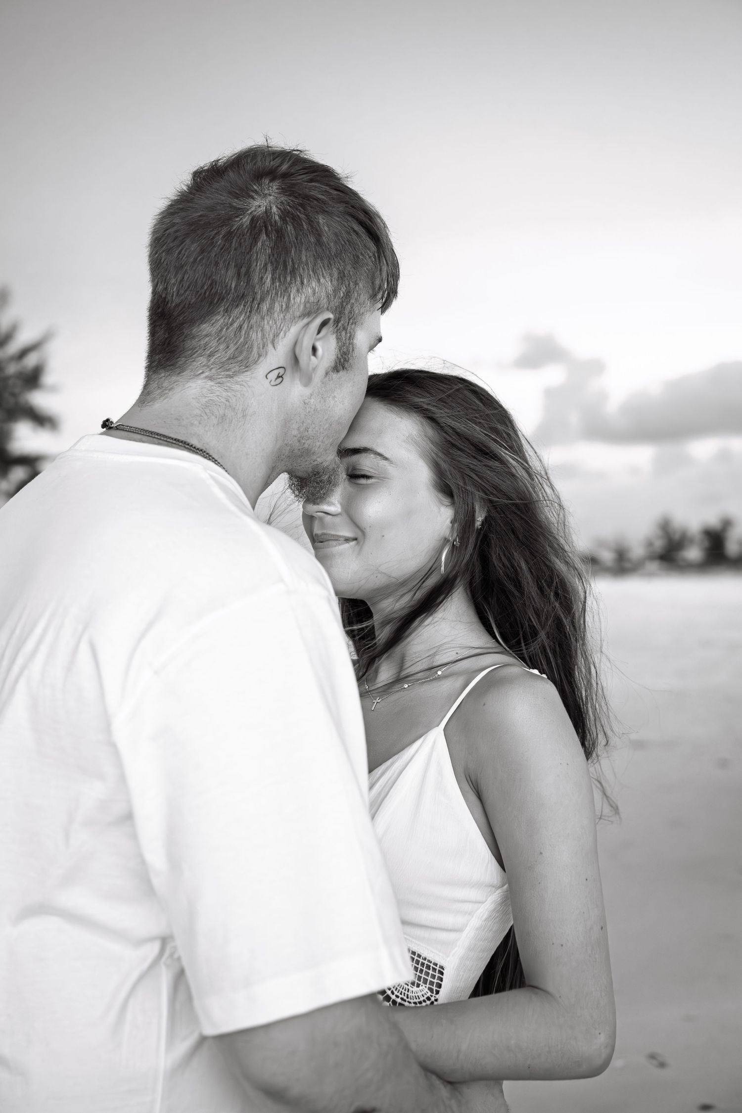 Black and white photo of a romantic couple embracing on a beach, woman smiling as man leans in close.