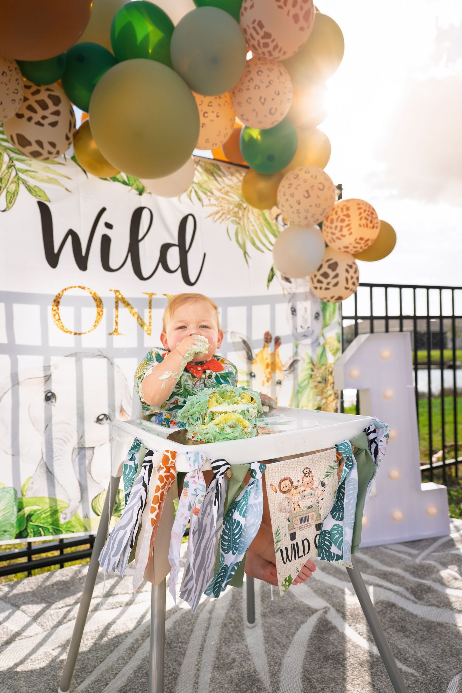 Outdoor party setup with pastel balloons and white chairs decorated under a covered patio space.