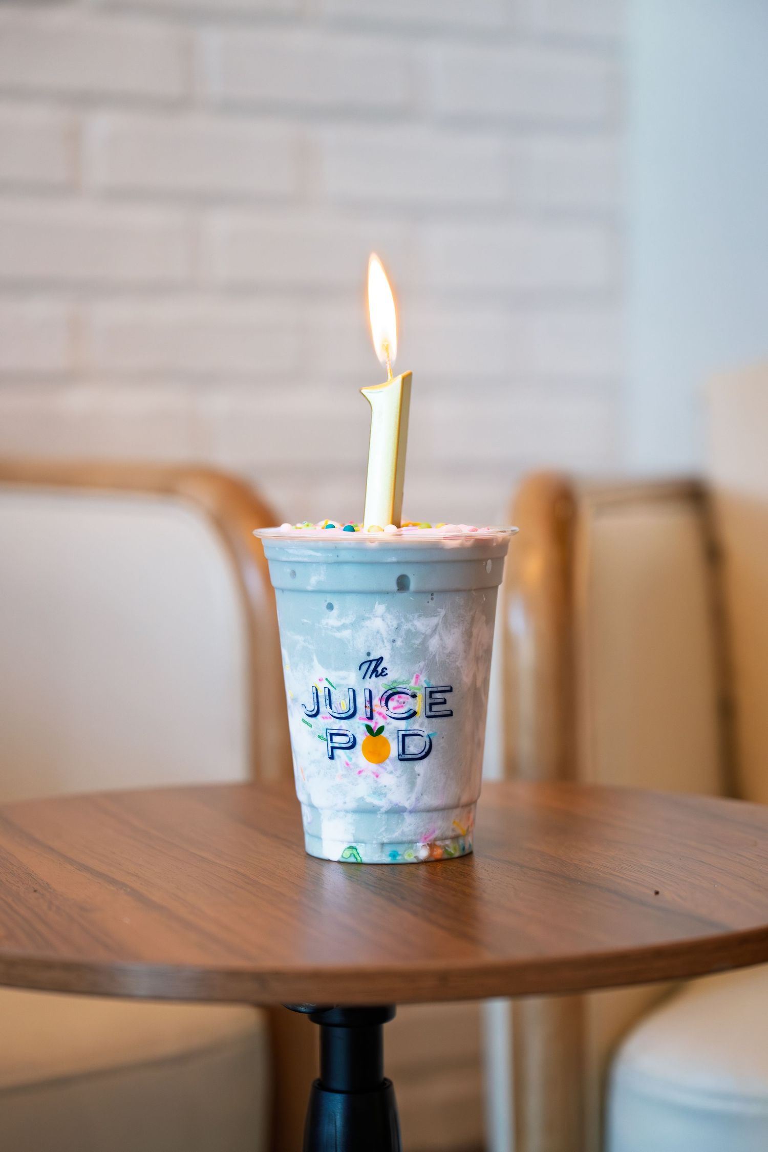 A birthday smoothie cup from The Juice Pod with a lit candle on a wooden table.
