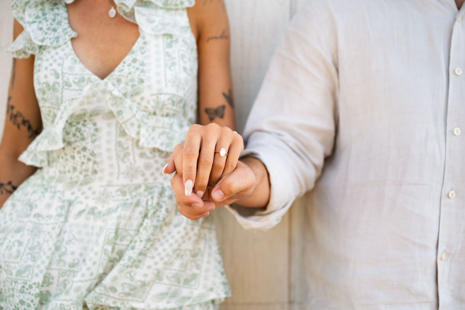 Close up view of hands exchanging rings during a wedding ceremony with floral dress and white shirt visible.