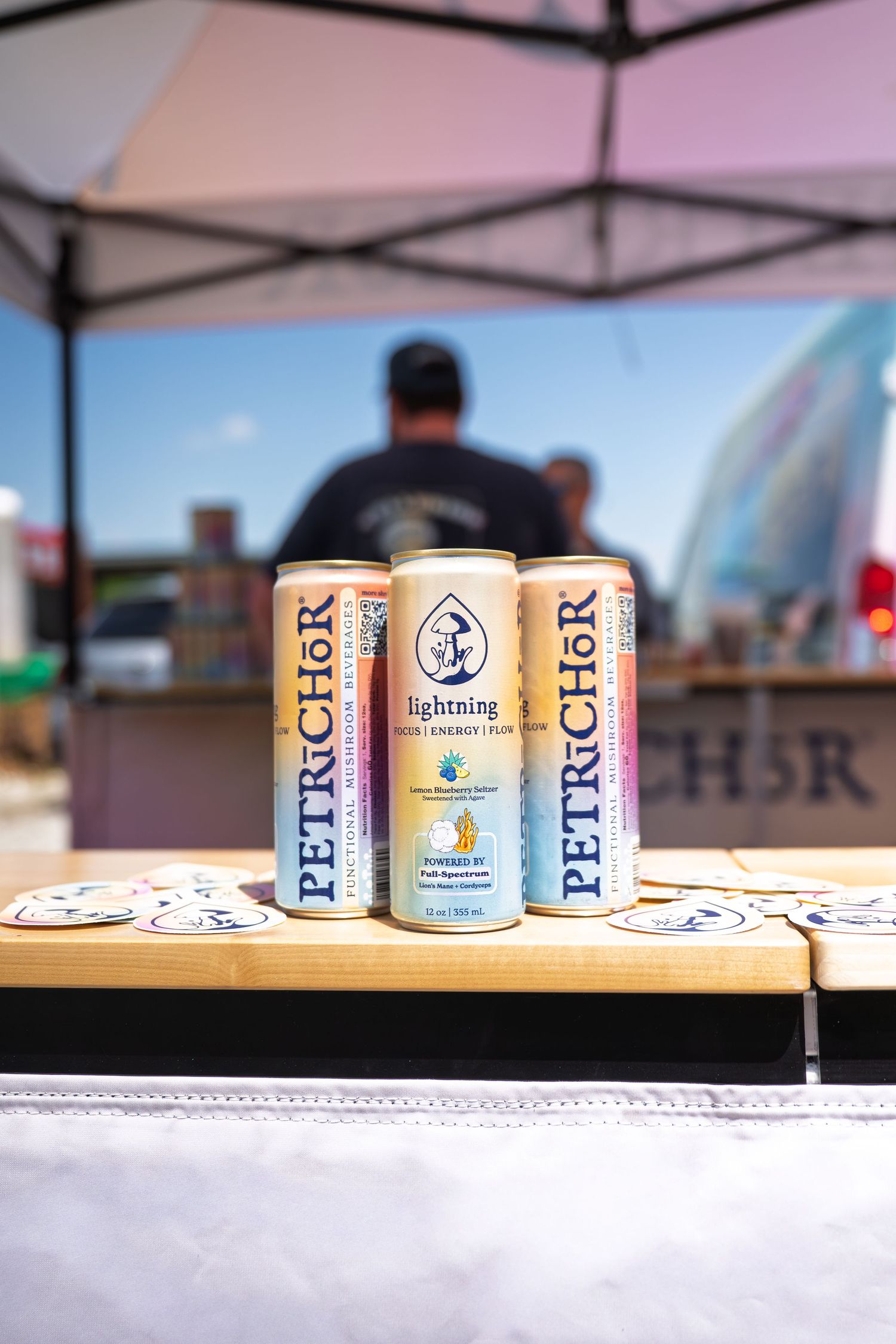Three PETRiCHoR Lightning energy drink cans displayed on a wooden table at an outdoor market event.