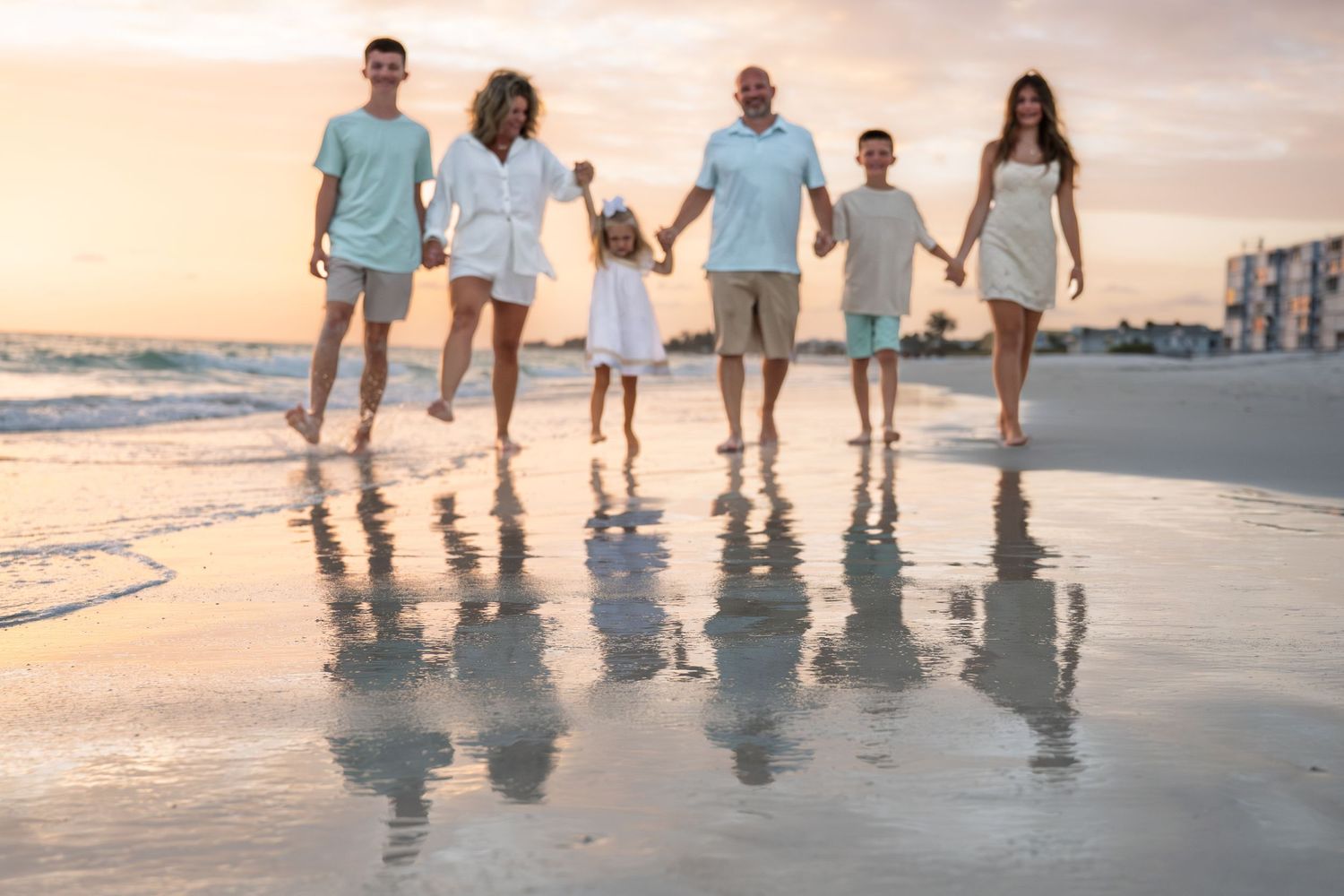 Family of six holding hands walking on a sandy beach at sunset with ocean waves in the background.