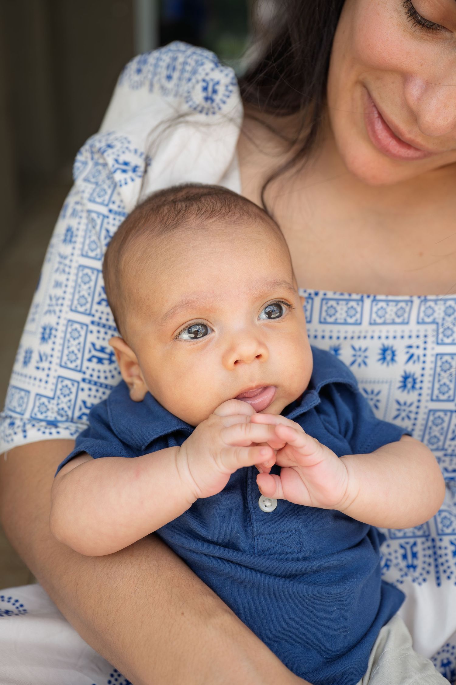 A mother in a blue floral dress tenderly holds her infant baby boy dressed in a navy blue onesie.