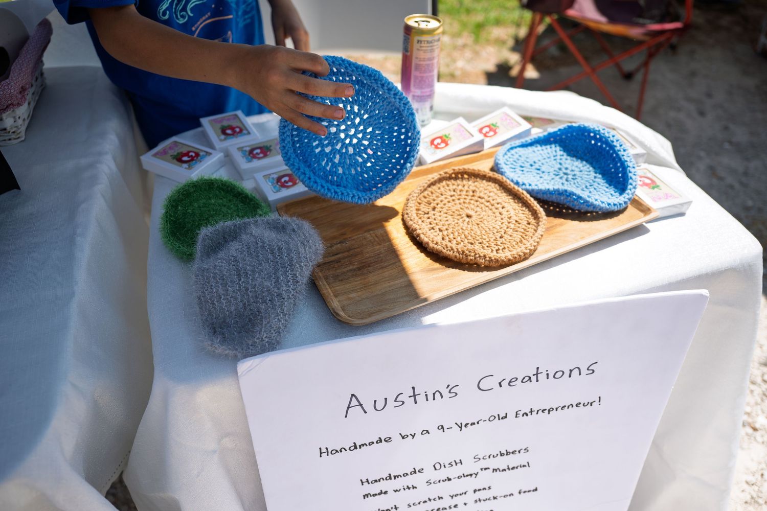 Young entrepreneur displays handmade crochet hats and coasters at Austin's Creations craft fair booth.