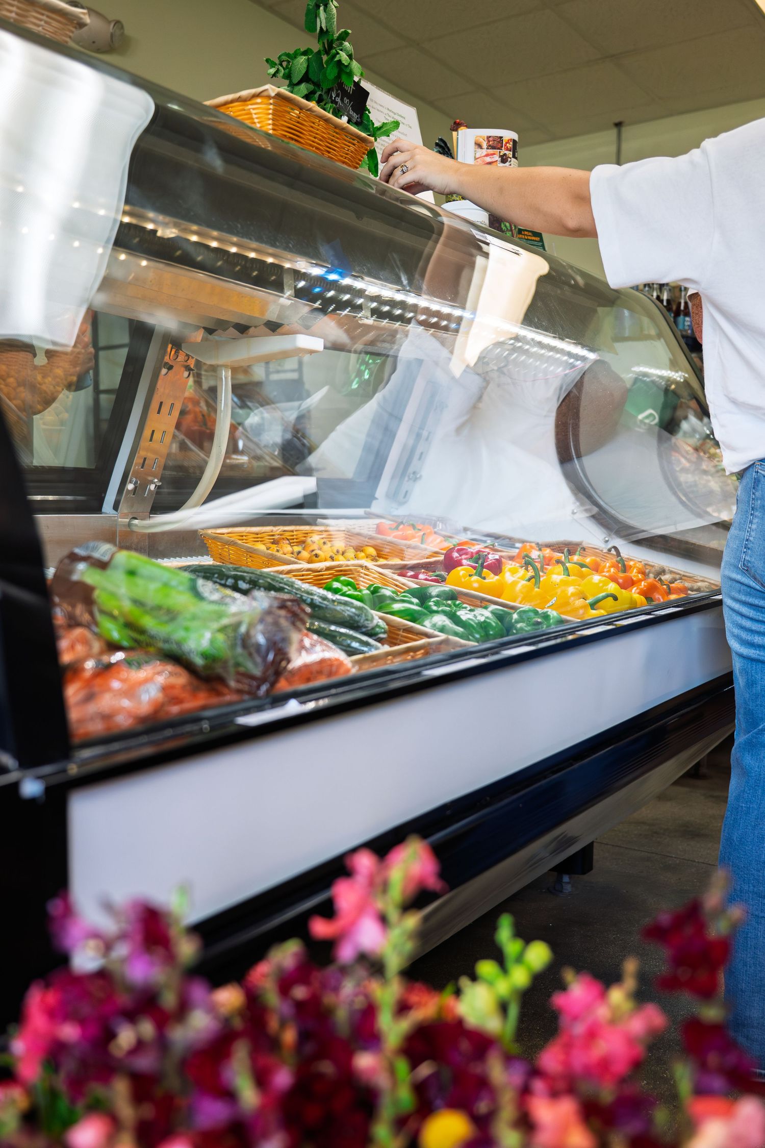 Colorful fresh food display case at a deli counter with a person serving food into a container.
