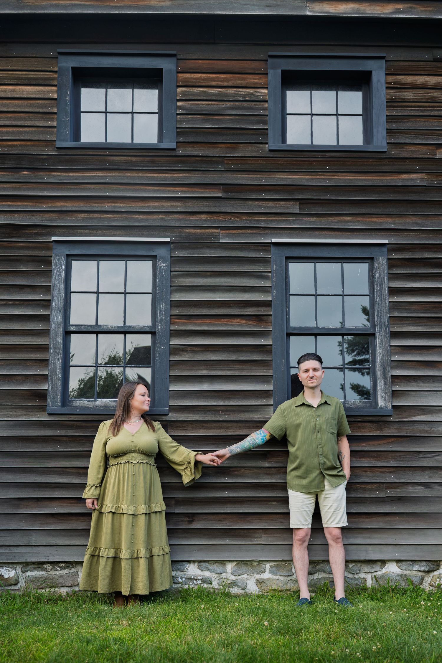 Couple holding hands in matching green outfits standing in front of a rustic wooden building with large windows.