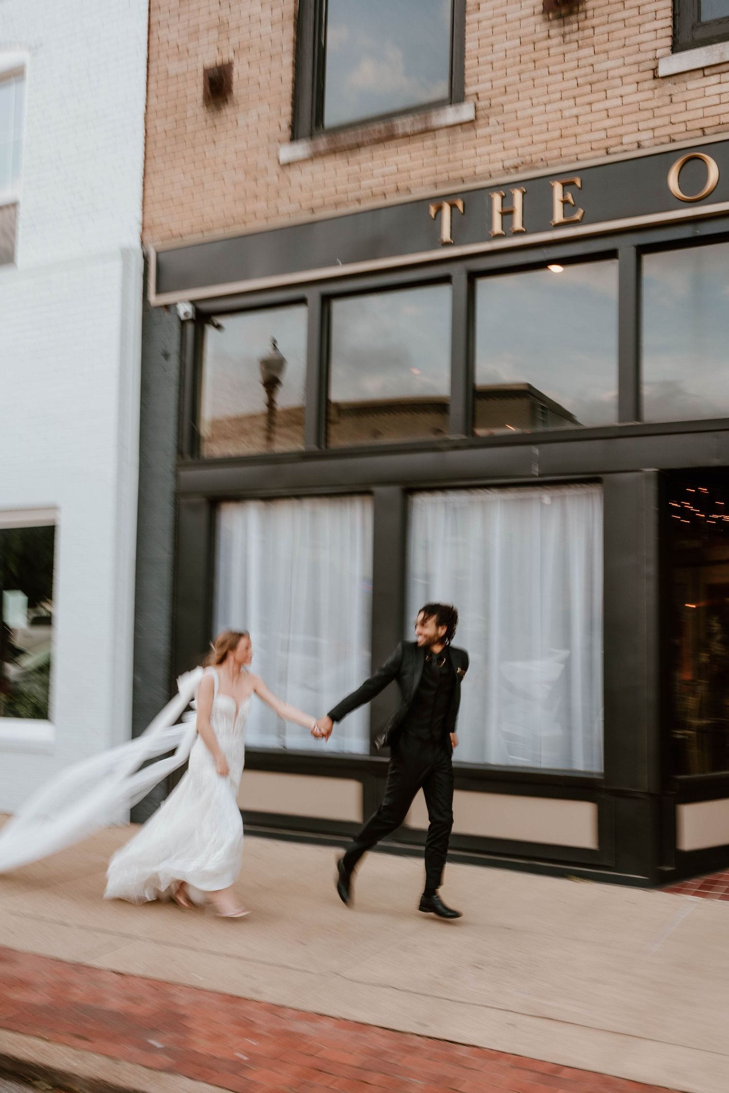 Newlyweds running hand in hand outside their wedding venue, captured with artistic motion blur and joyful movement.