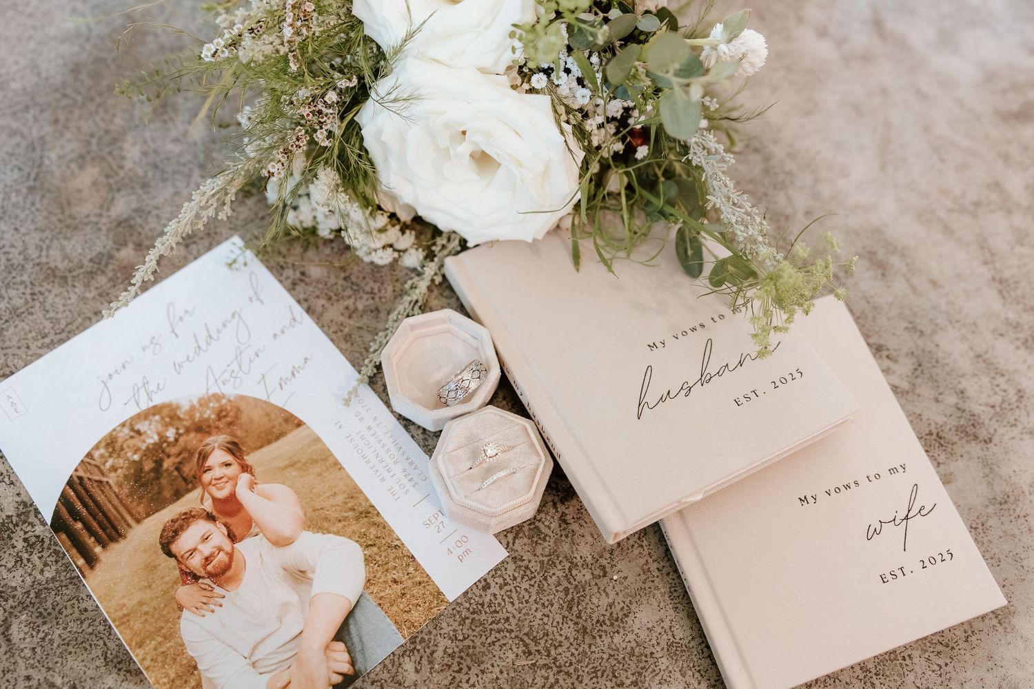 Wedding details featuring invitation suite, bridal bouquet, vow books, and wedding rings styled for a romantic celebration