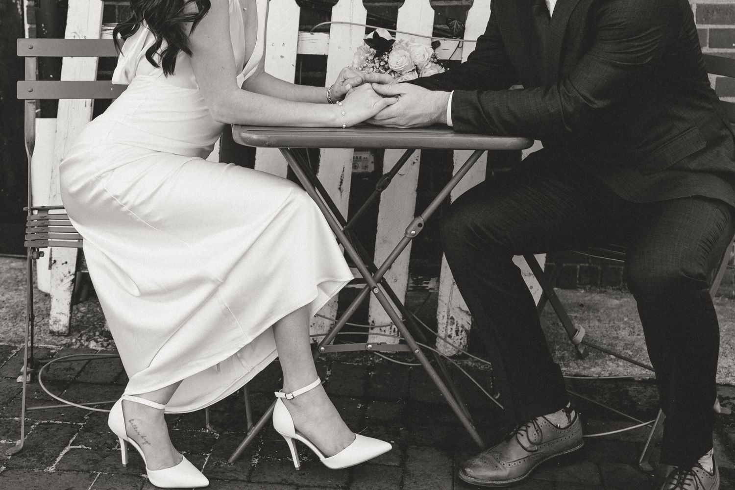 Black and white wedding portrait of newlyweds holding hands across a café table. Fort Campbell Clarksville solider elopement courthouse