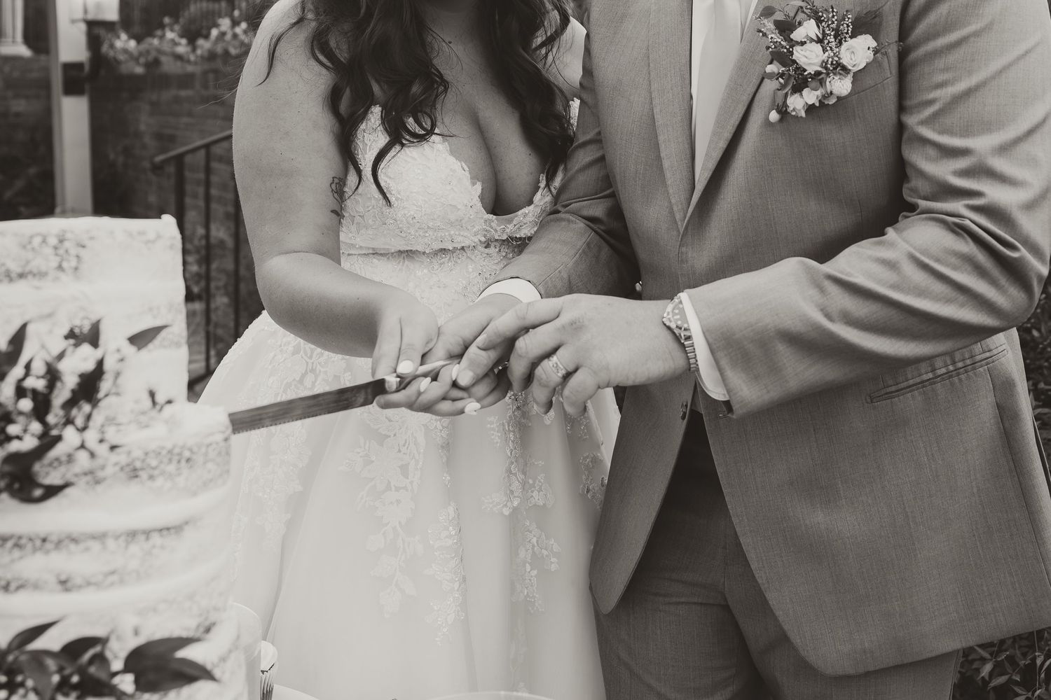 Black and white wedding photo of newlyweds cutting their wedding cake during a joyful reception celebration.