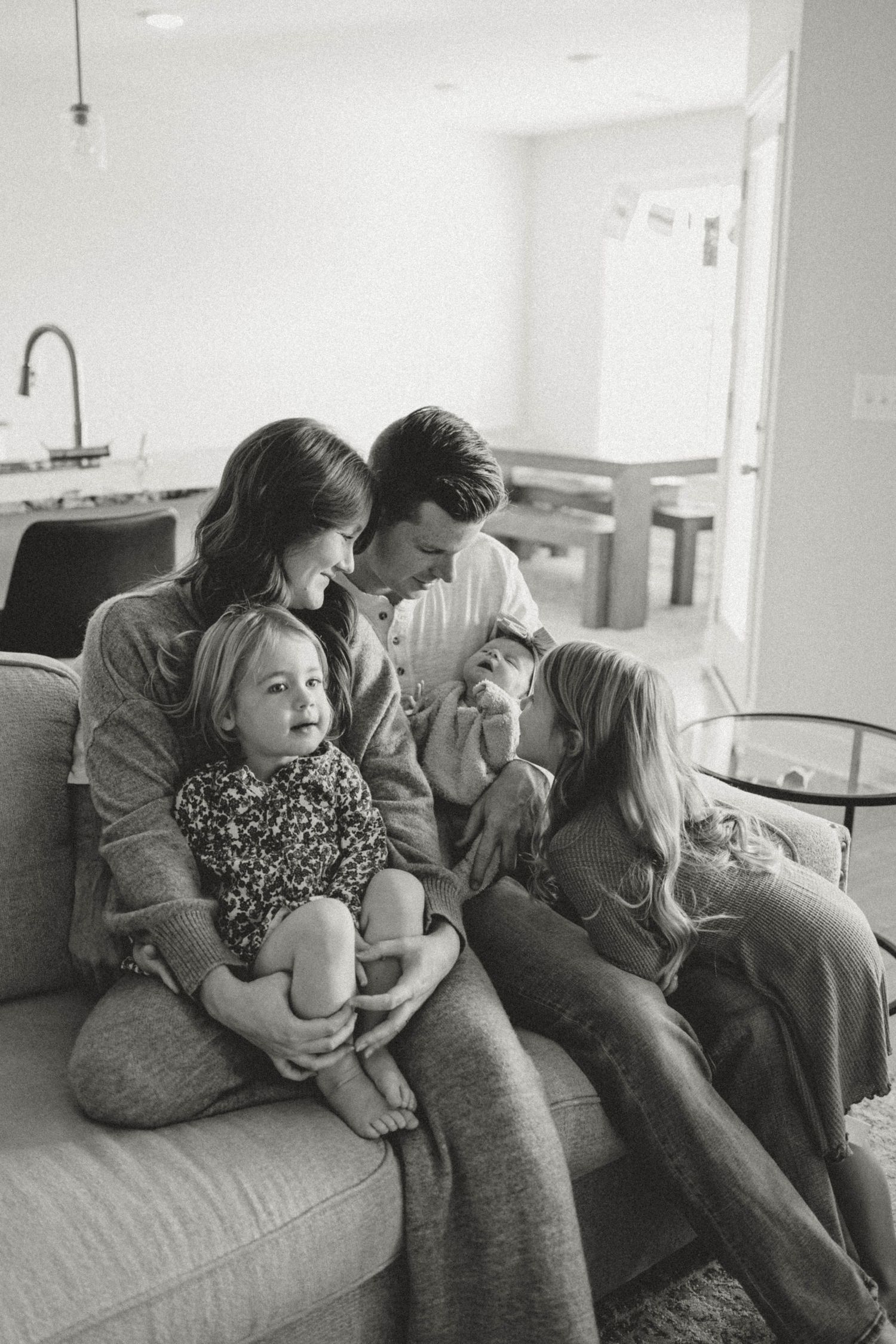 Candid black and white family photo with parents and siblings looking at a newborn baby. fort campbell, kentucky. army base post