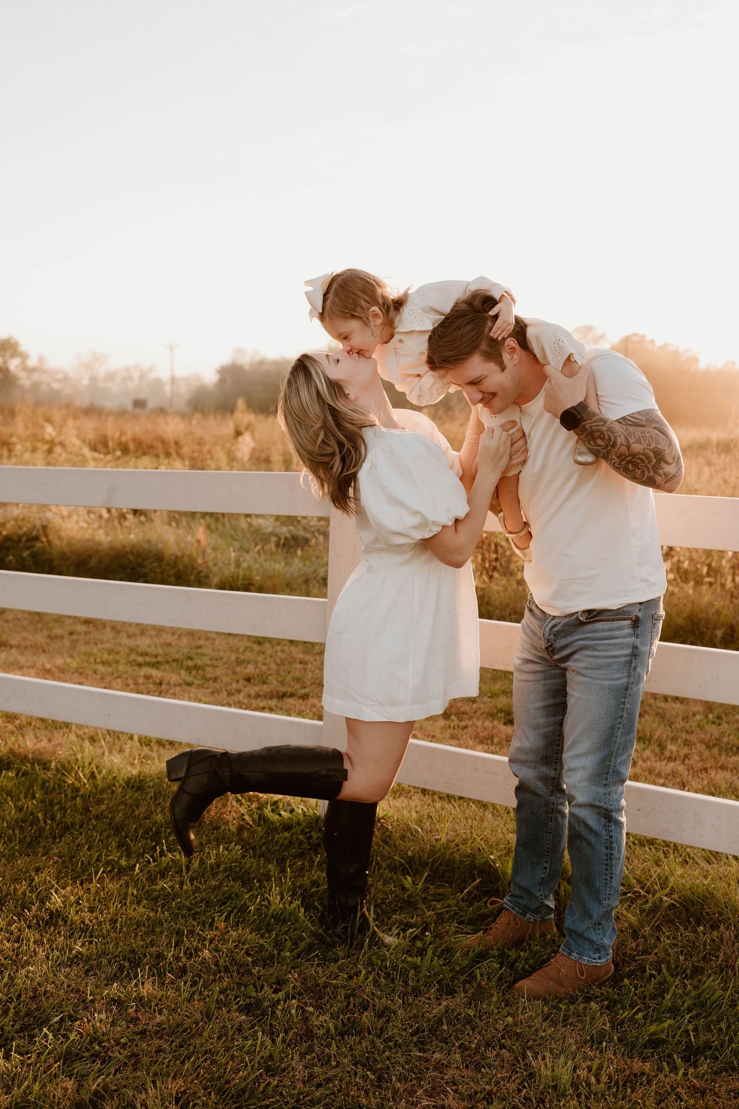 Family maternity announcement session at Valor Hall in Clarksville, TN, with parents sharing a kiss holding their daughter at golden hour