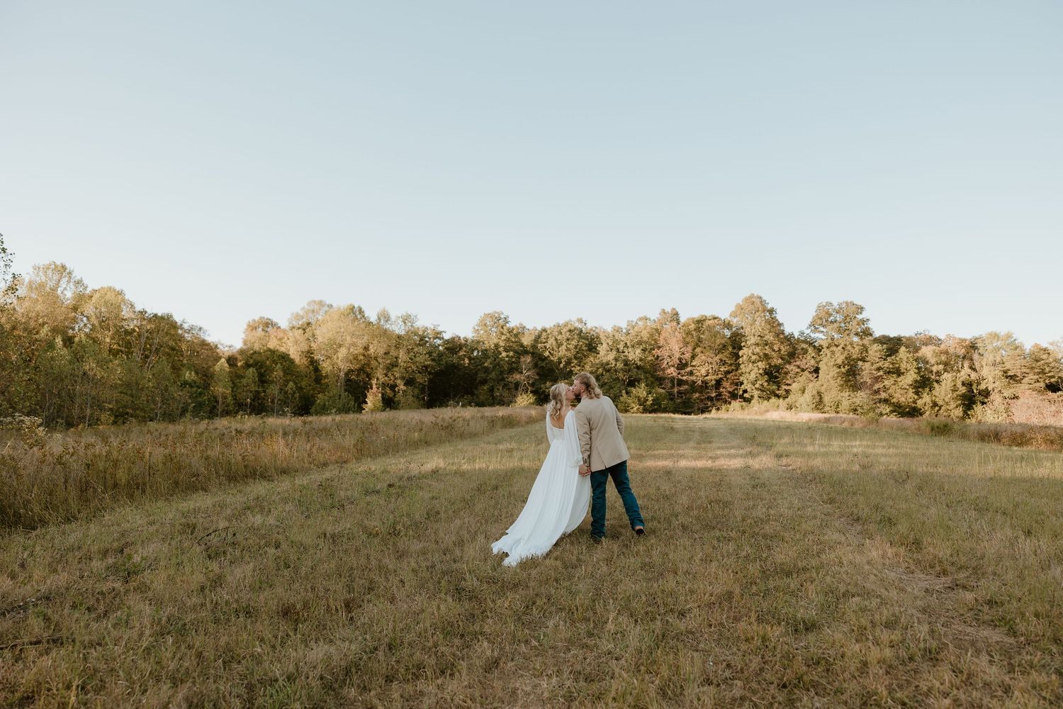 Bride and groom sharing a kiss in an open field during a romantic Tennessee wedding surrounded by natural scenery.