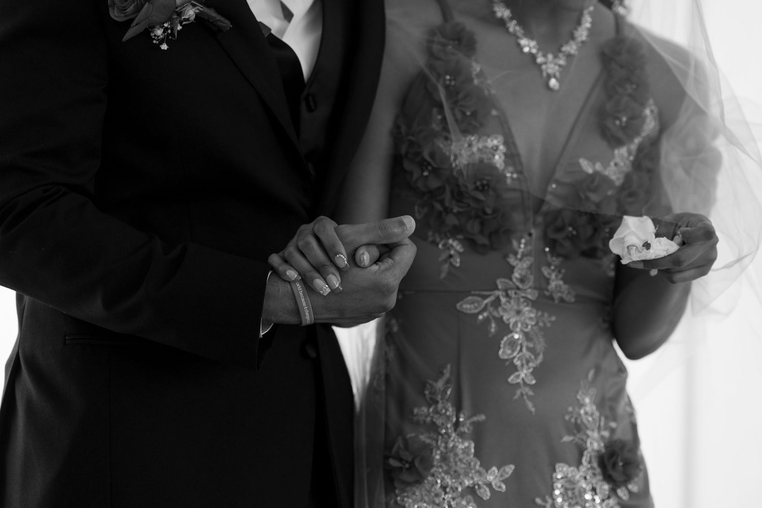 A black and white close-up of a bride and groom holding hands during their wedding ceremony.