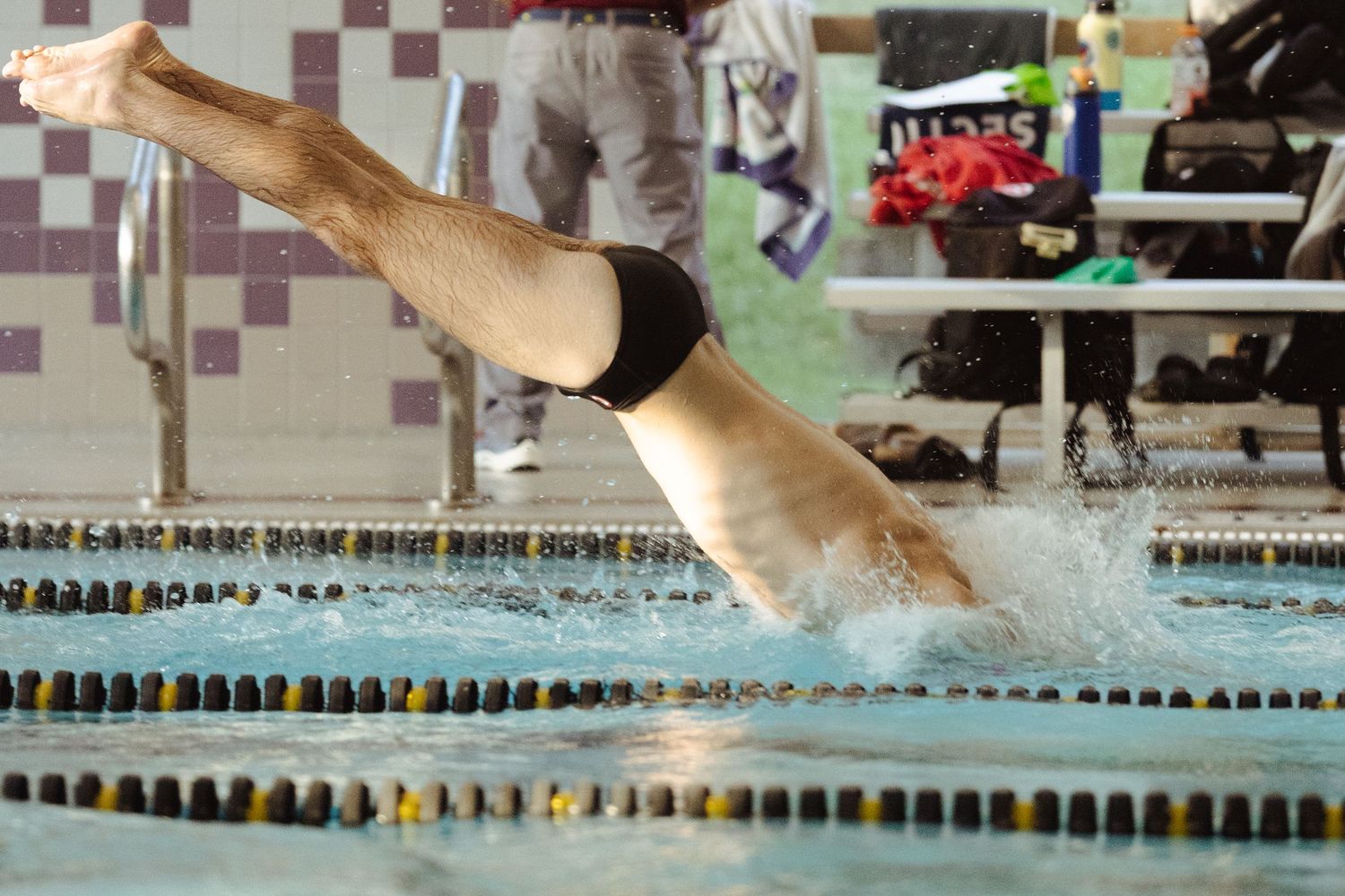 Competitive swimmer diving into indoor pool lane during swim meet competition.