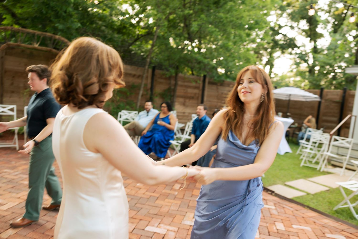 Bride and bridesmaid in blue dress dancing together at an outdoor wedding reception.