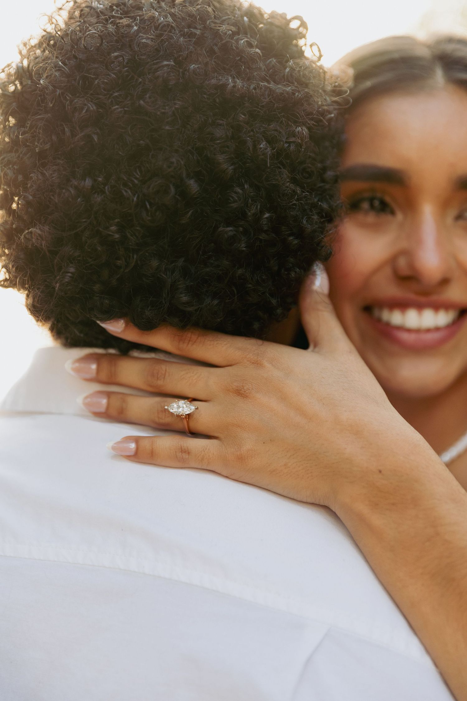 Smiling bride hugging groom, showcasing a diamond engagement ring on her finger during a romantic wedding moment.