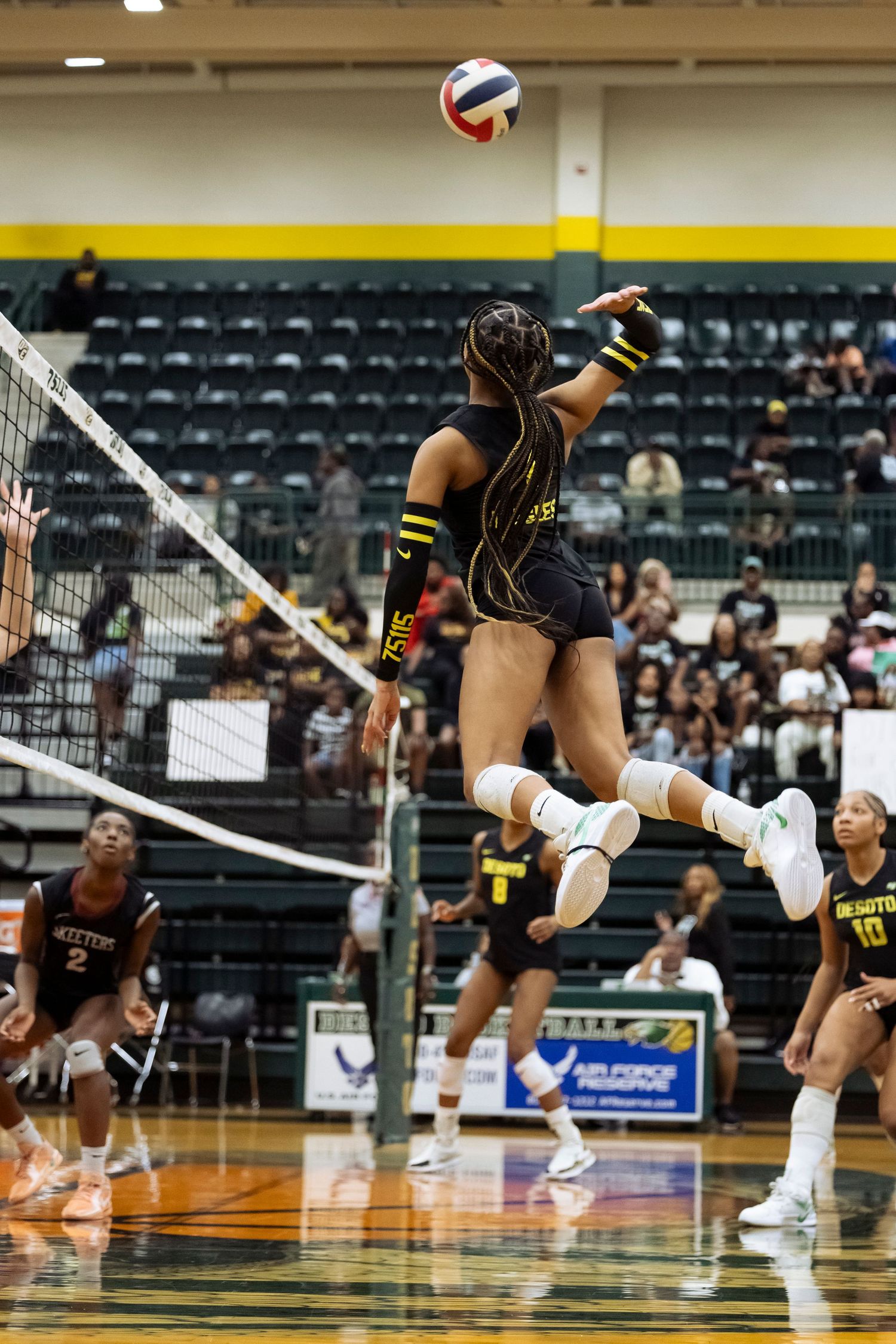 Volleyball player in black uniform leaps to spike the ball over the net during a competitive match.