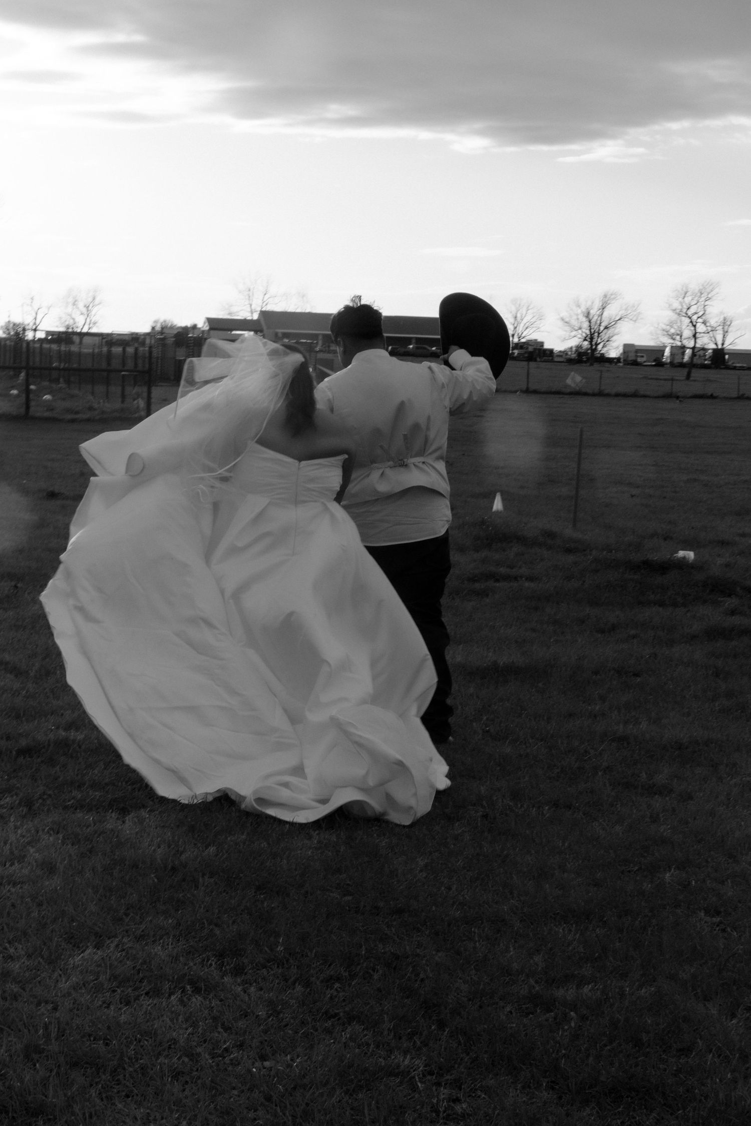 Black and white photo of bride and groom dancing in an open field with wedding dress flowing in the wind.