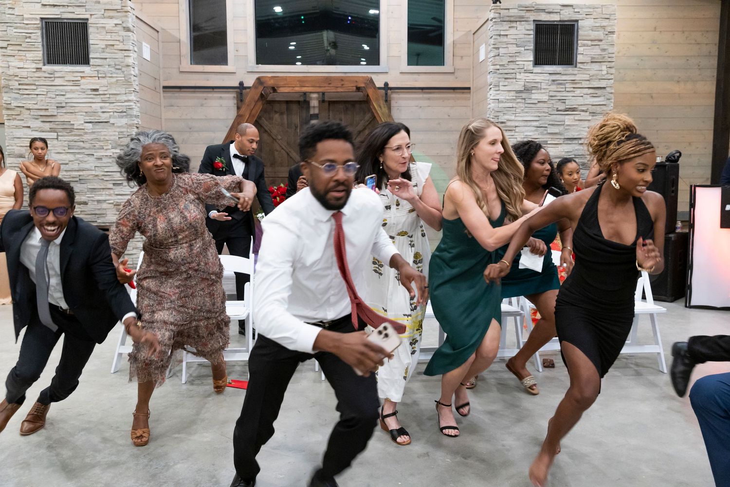 Energetic wedding guests perform a lively group dance at an indoor wedding reception.