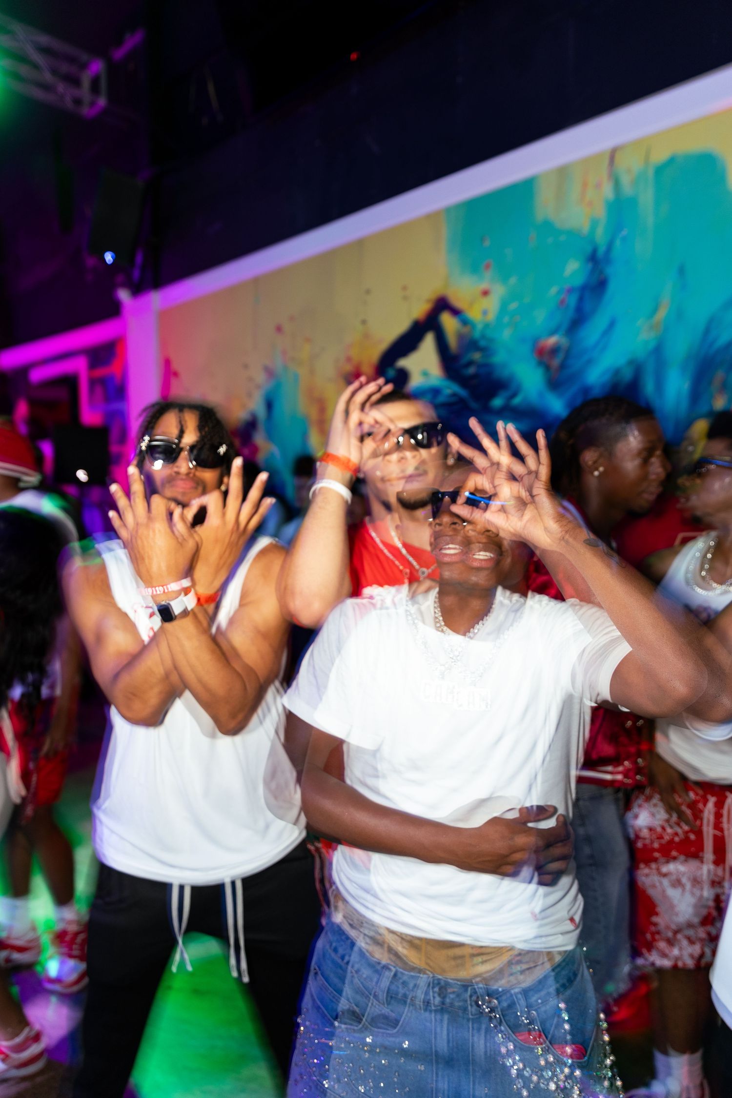 Group of friends posing and dancing at a colorful indoor party event wearing white outfits.
