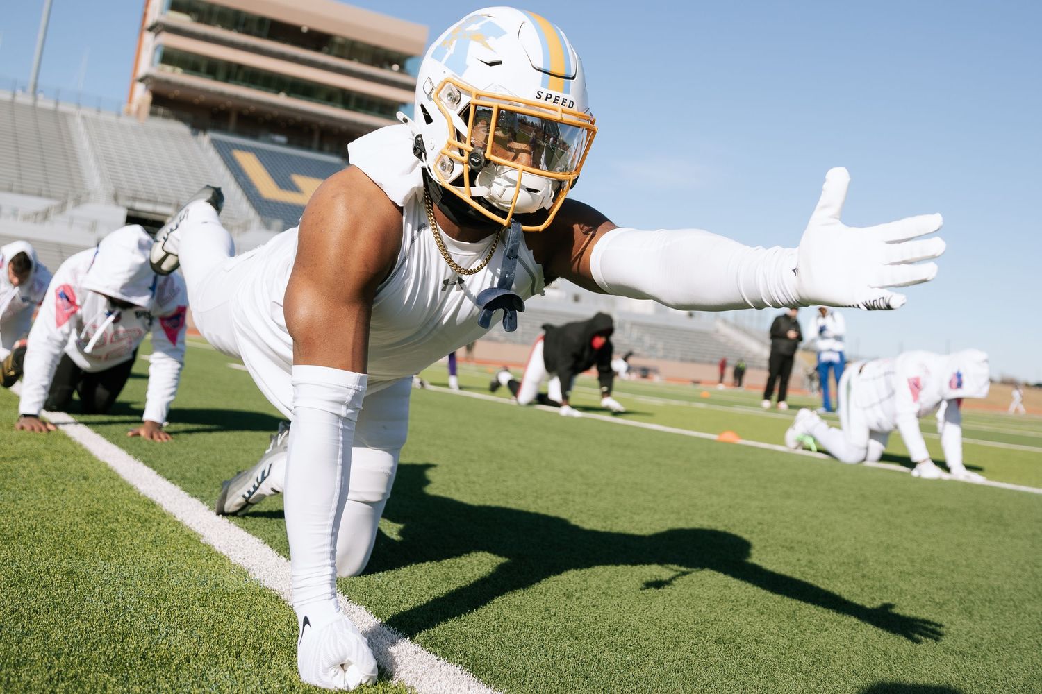 Football player in gold uniform stretching in push-up position on stadium turf before game.