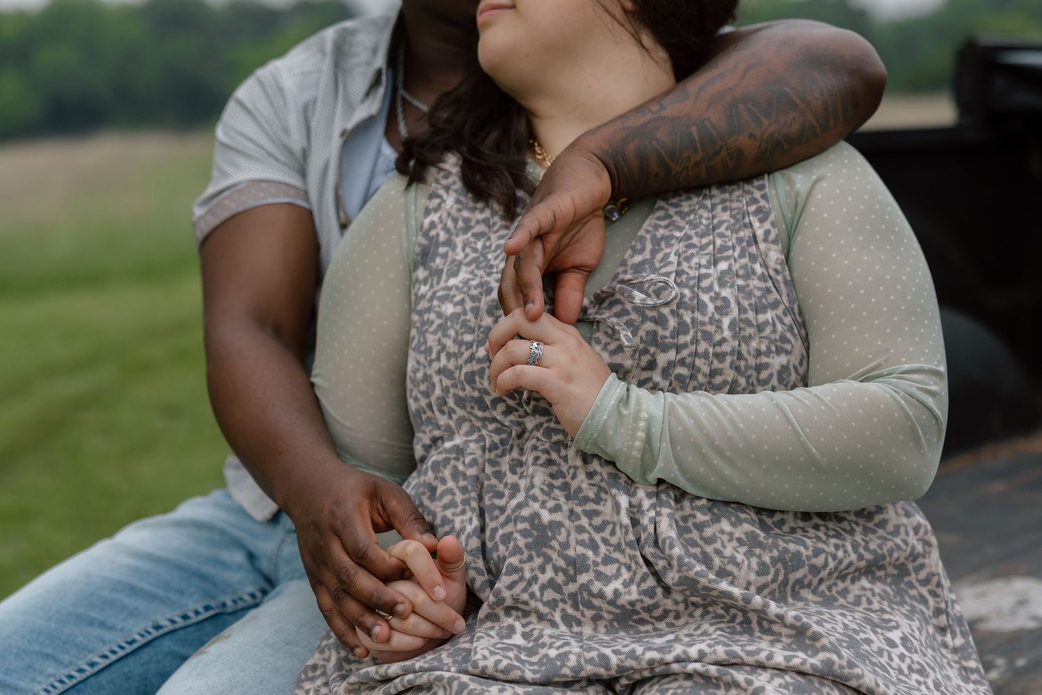 Close-up of an interracial couple holding hands, man with tattooed arm embracing woman in floral dress.
