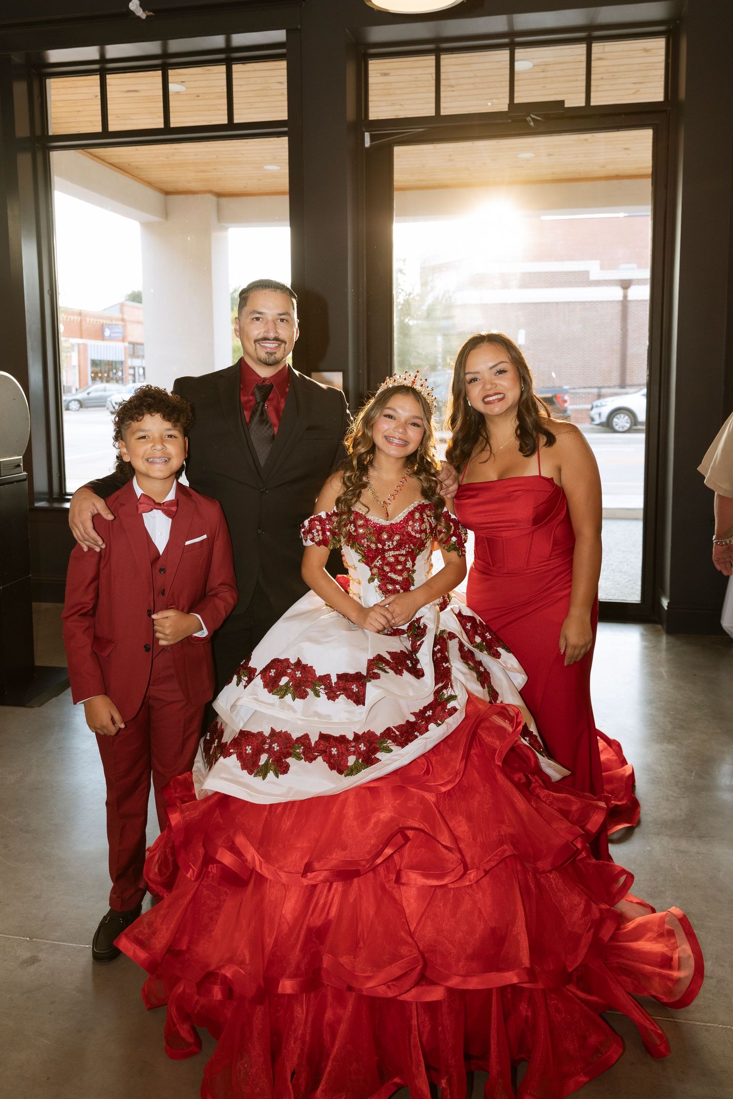 Family of four posing together at a quinceañera celebration with the birthday girl in a red and white ballgown.