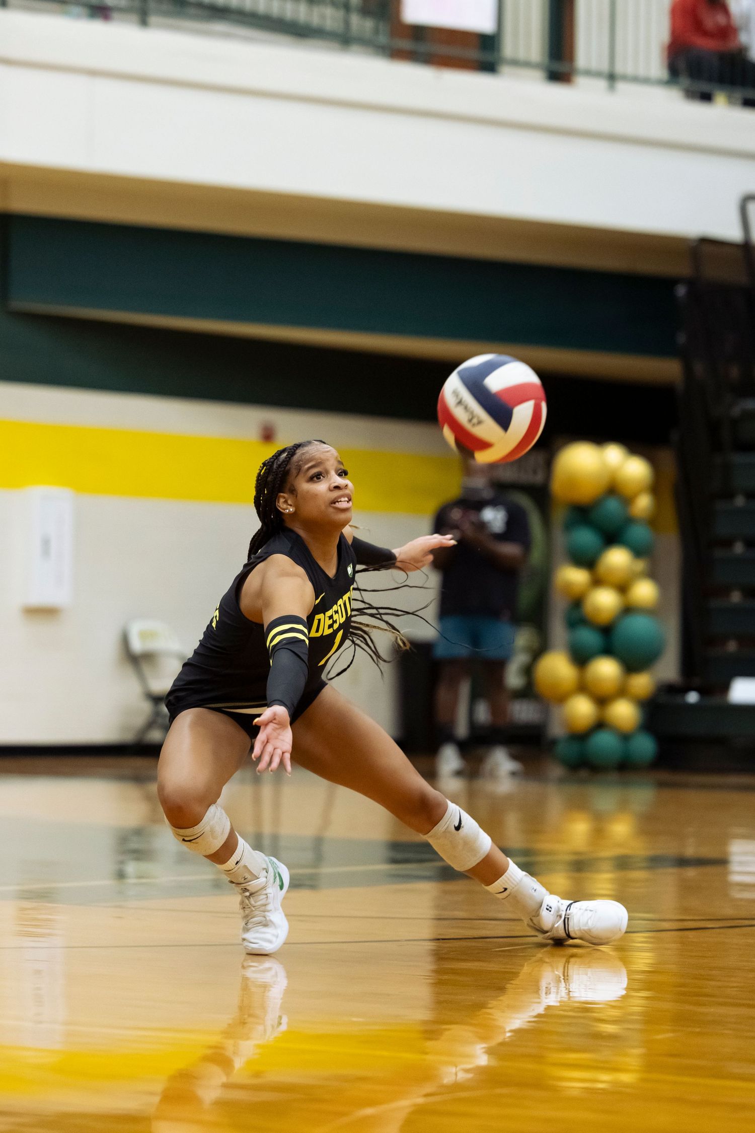 Female volleyball player in black uniform dives low to dig the ball during an indoor match.