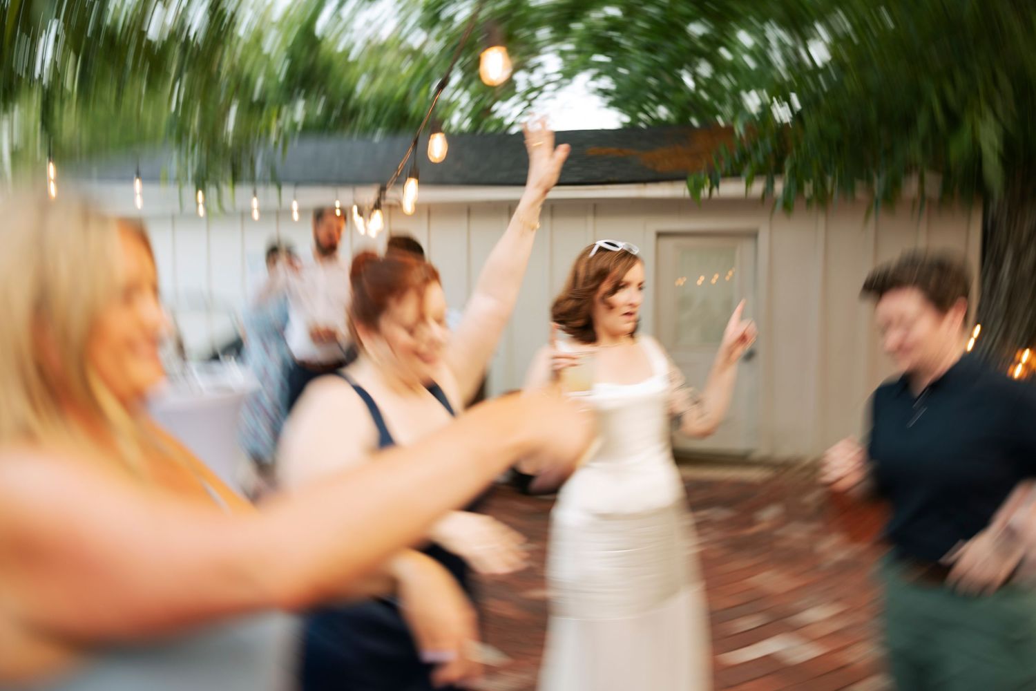Bride dancing joyfully with guests at a lively outdoor wedding reception.