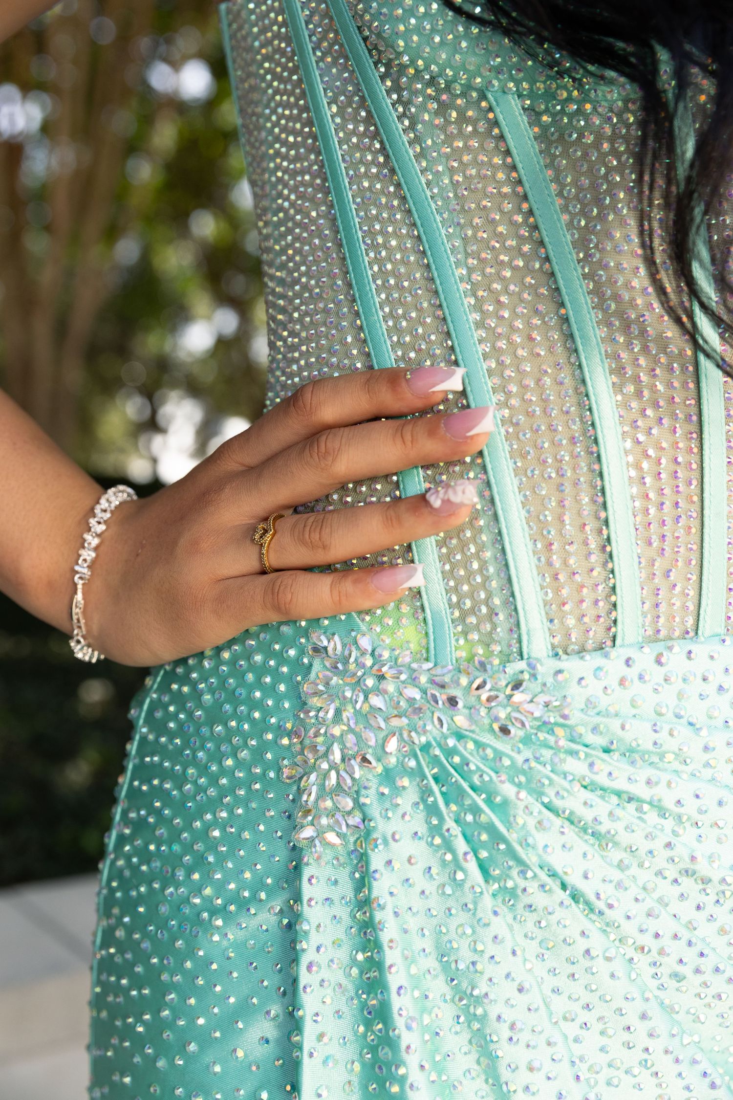 Close-up of a teal beaded prom dress with rhinestone embellishments and a manicured hand.
