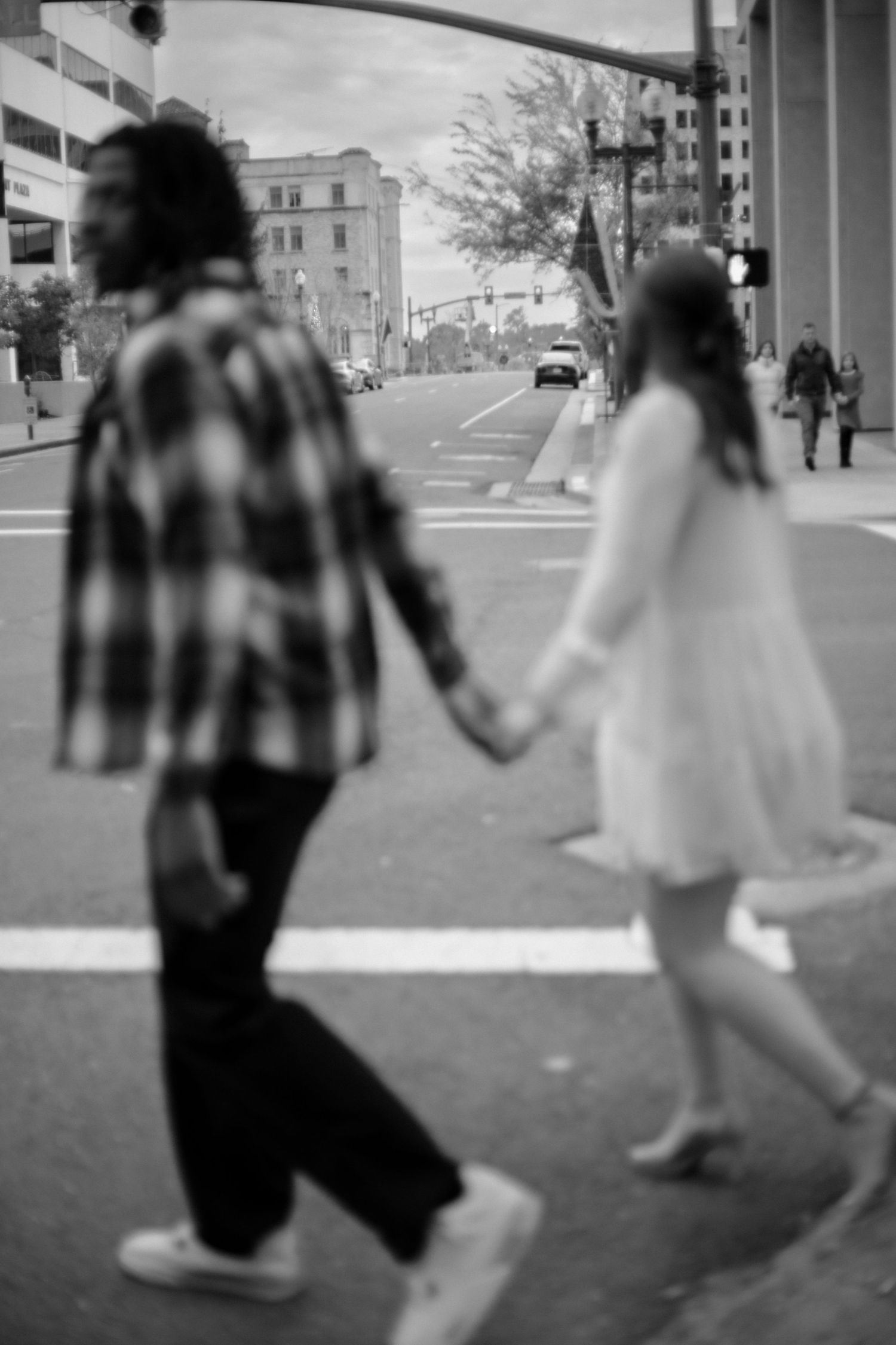 Black and white photo of a couple holding hands while crossing a street in an urban setting.