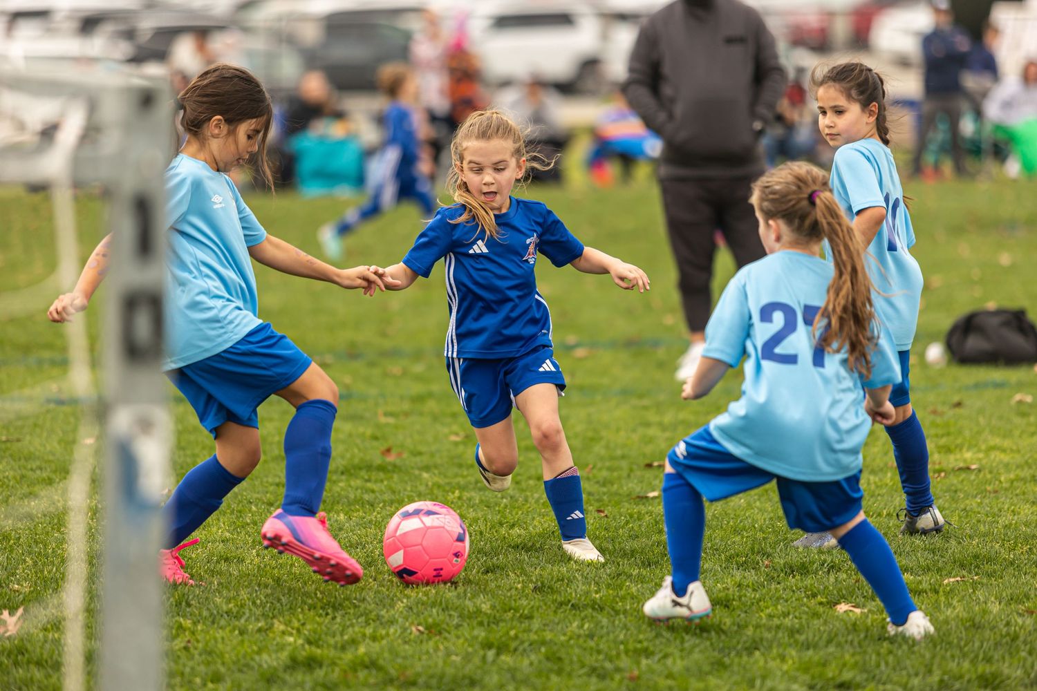 Young girls playing youth soccer in blue uniforms competing for pink ball on green grass field.
