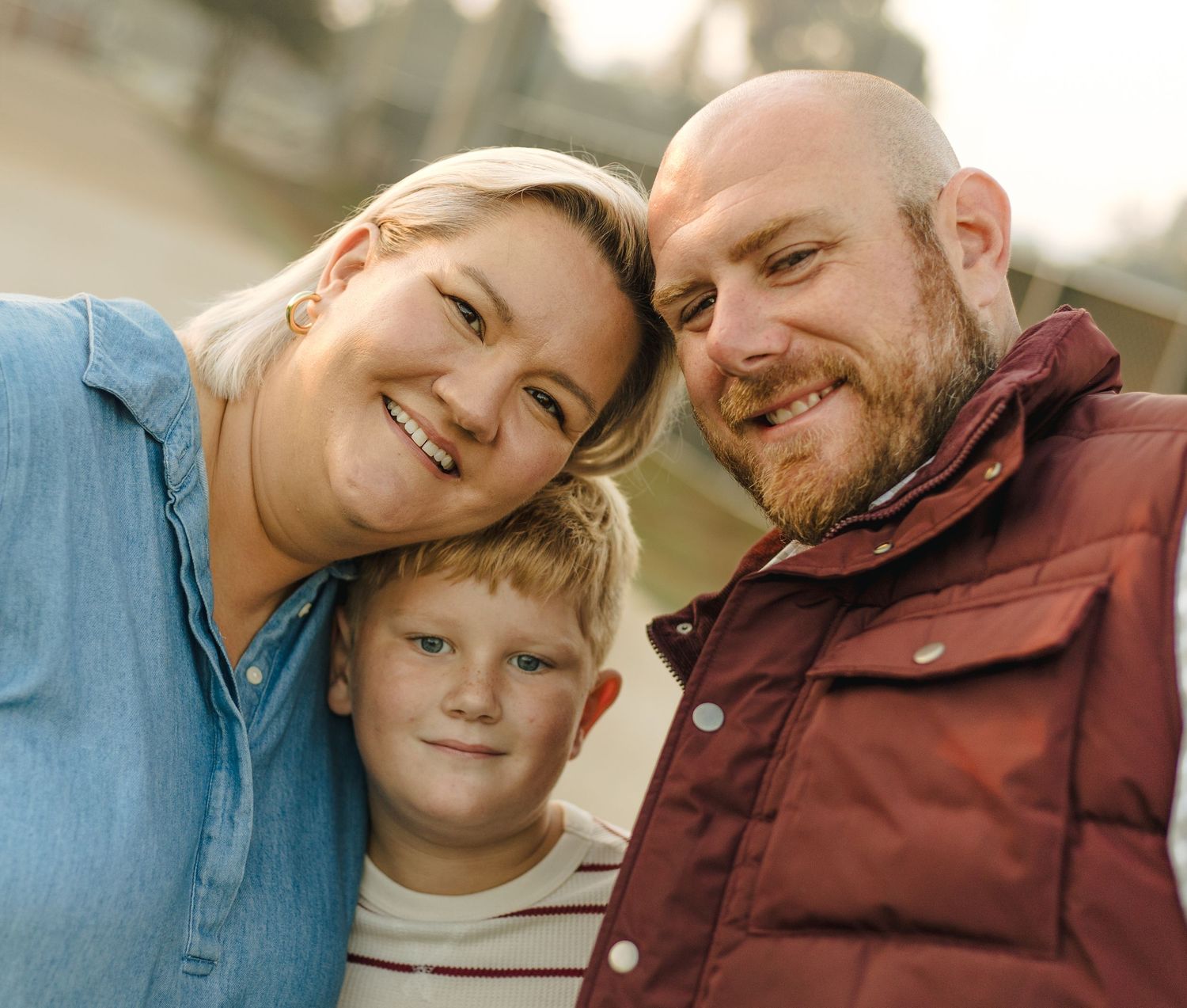 Happy family portrait of parents and young son smiling closely together outdoors.