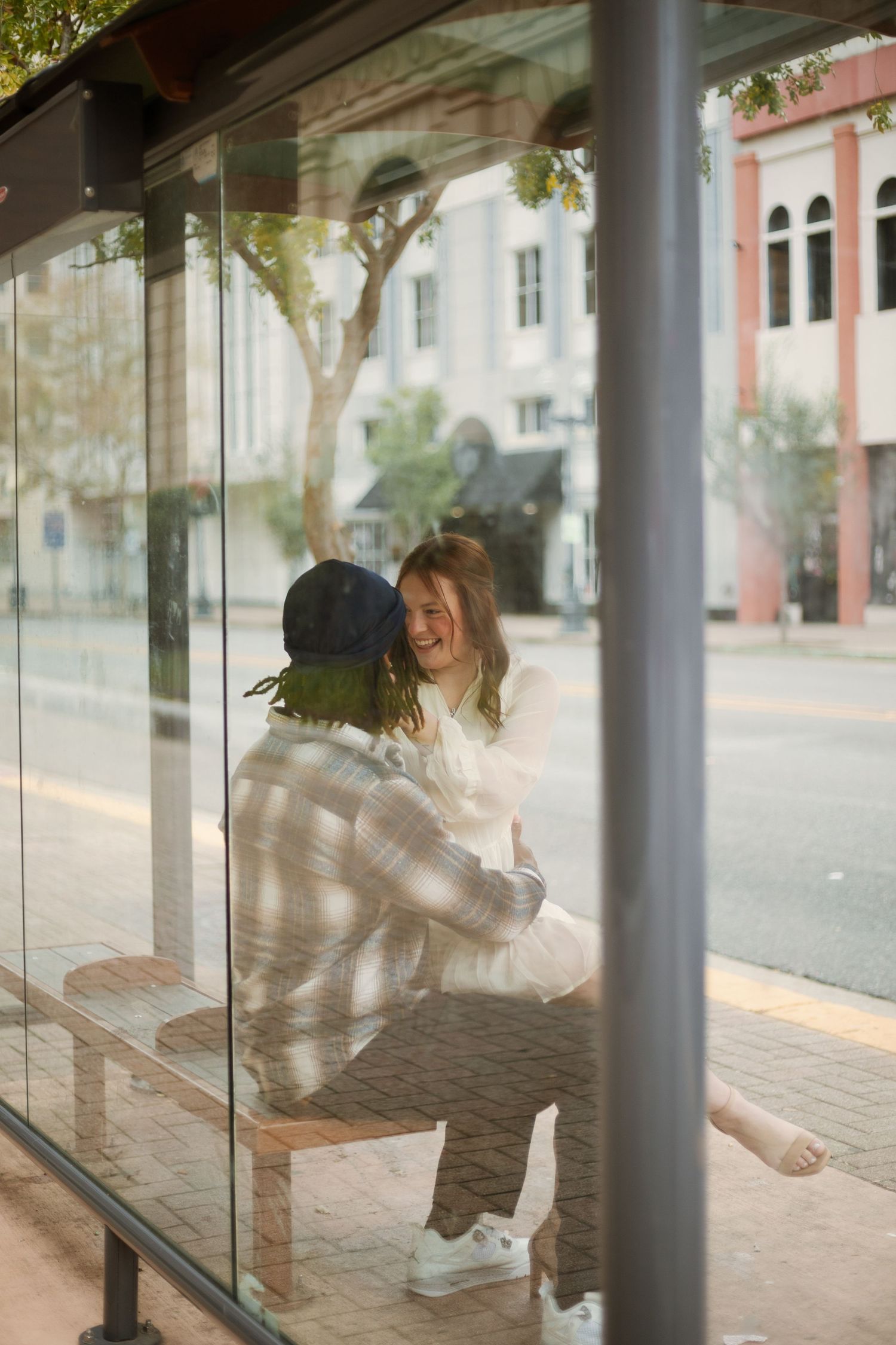 Happy couple laughing together at a glass bus stop shelter on a city street.