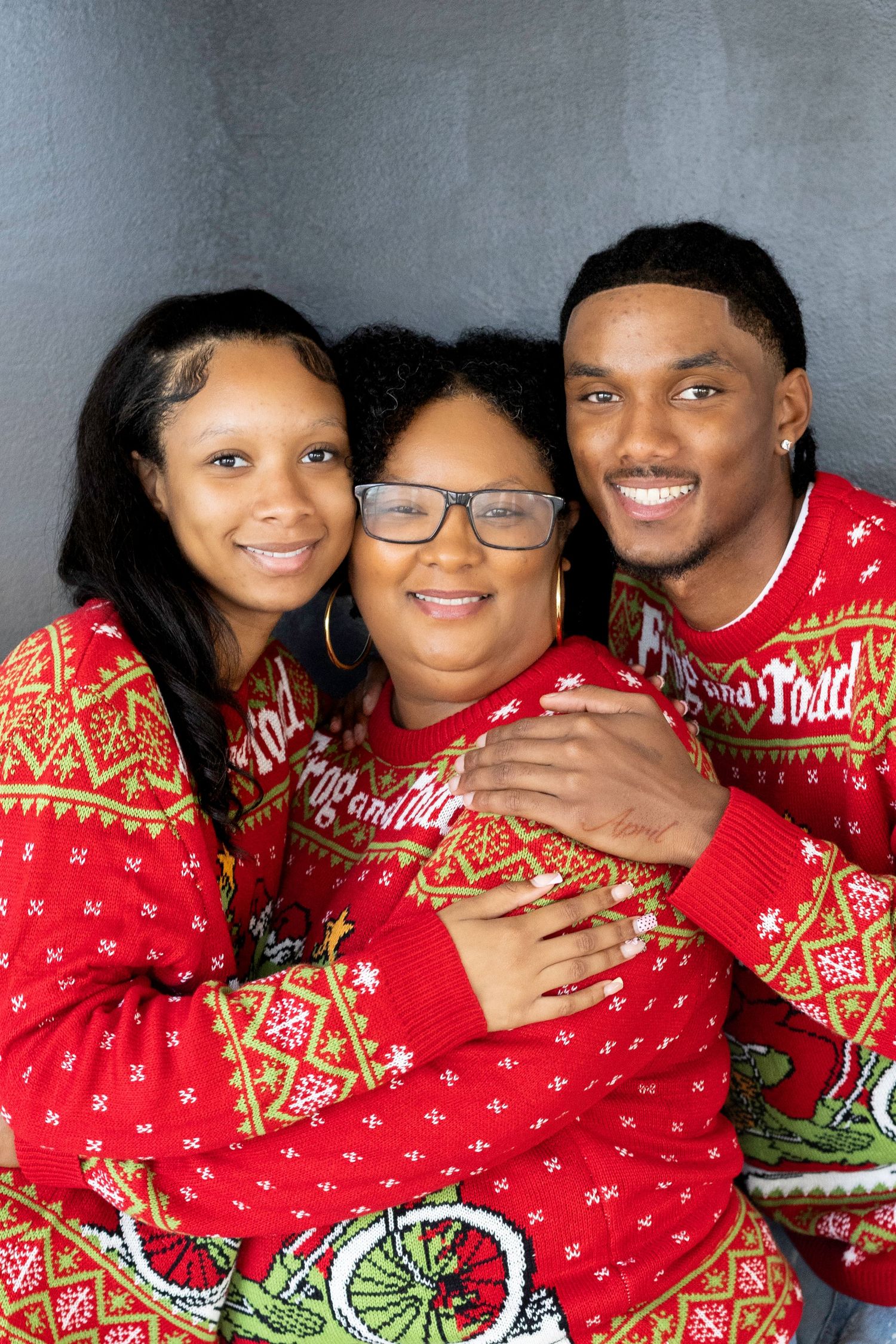 Family of three wearing matching red Christmas ugly sweaters smiling together for a holiday portrait.