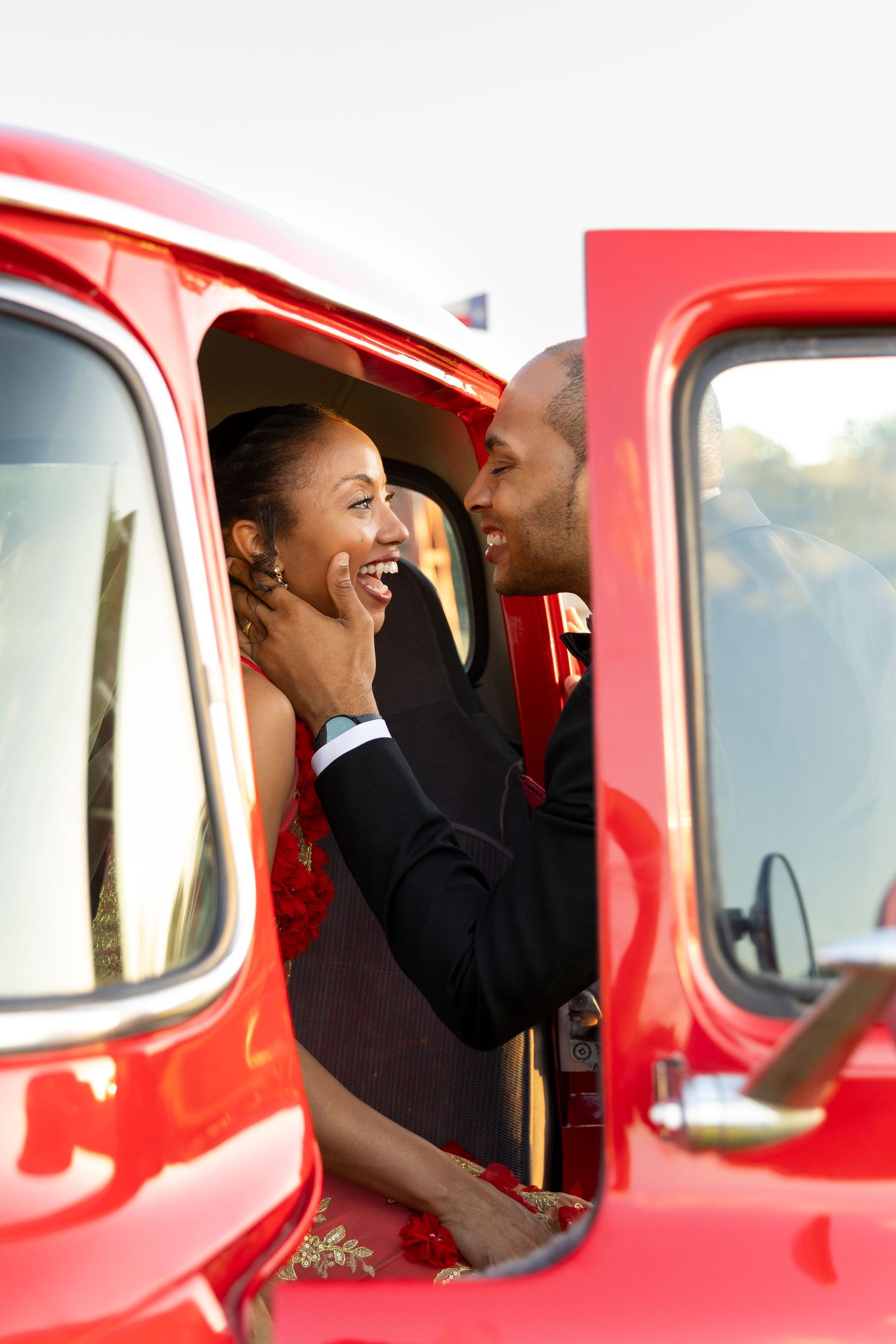 A joyful couple shares a romantic moment inside a vintage red truck on their wedding day.