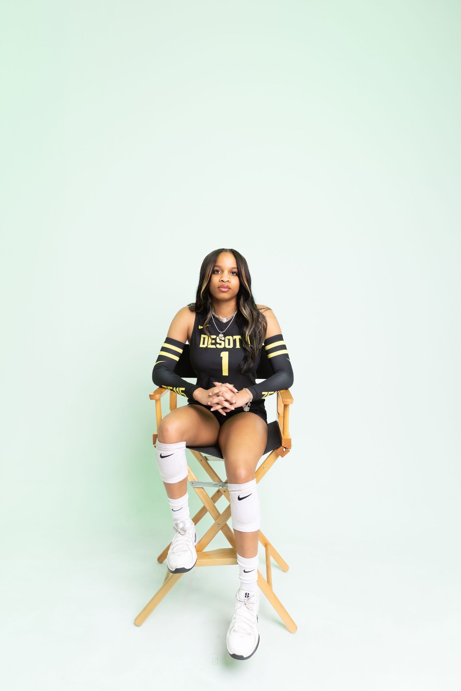 Female volleyball player wearing DeSot jersey number 1 sits in director's chair against mint green background.